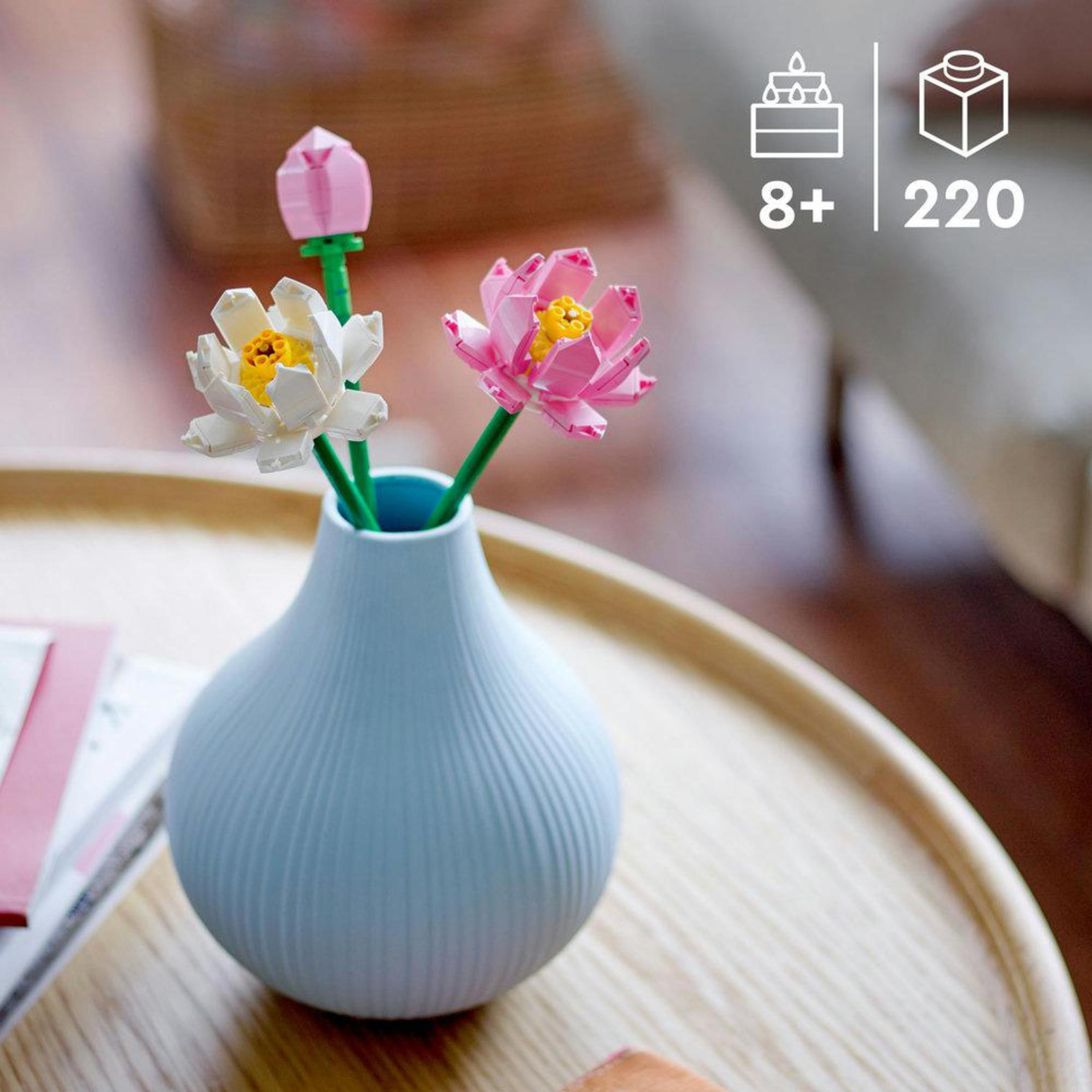 Un vaso blu con tre fiori Lego su un tavolo di legno.