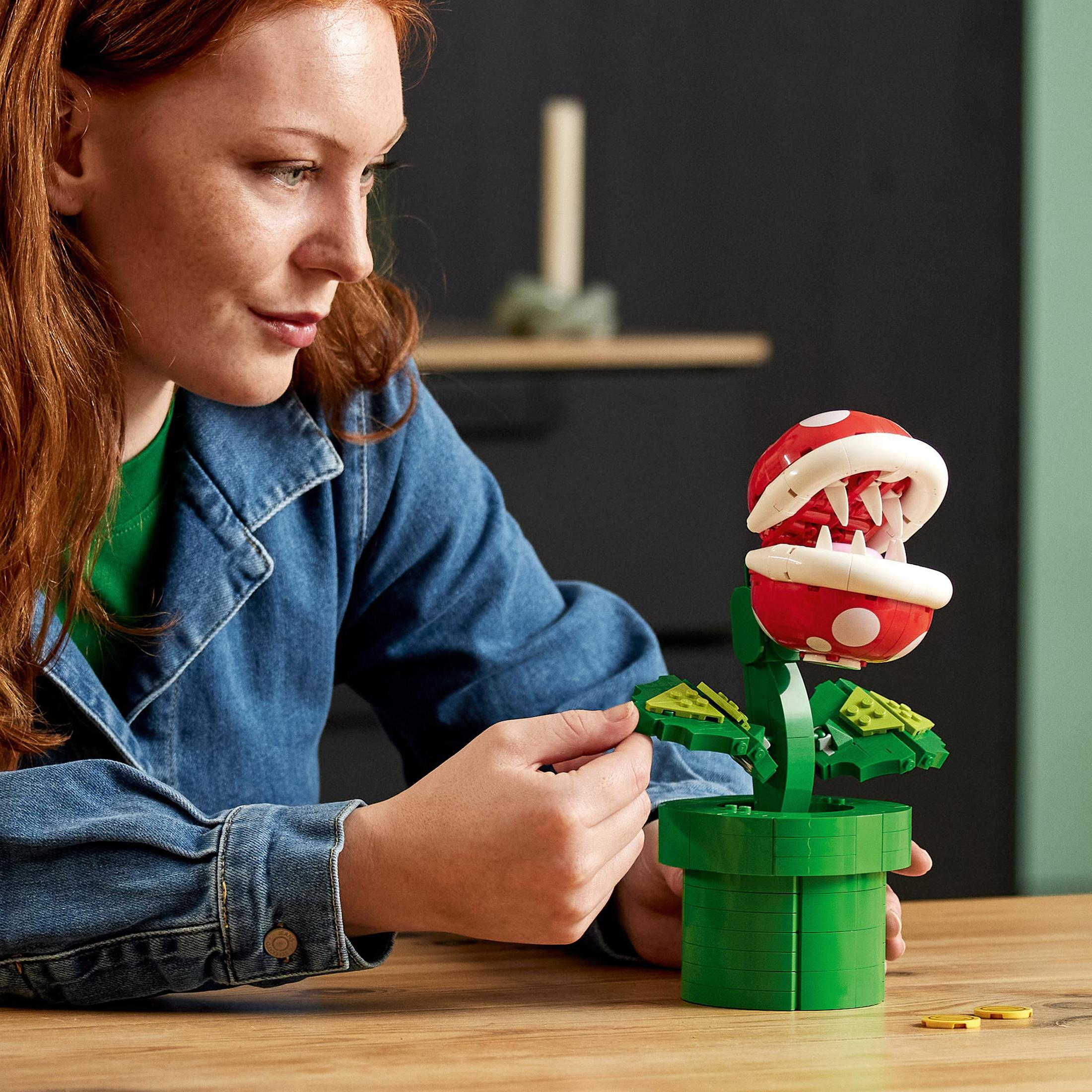 Donna dai capelli rossi gioca con la pianta Piranha LEGO, vaso e pianta verdi.