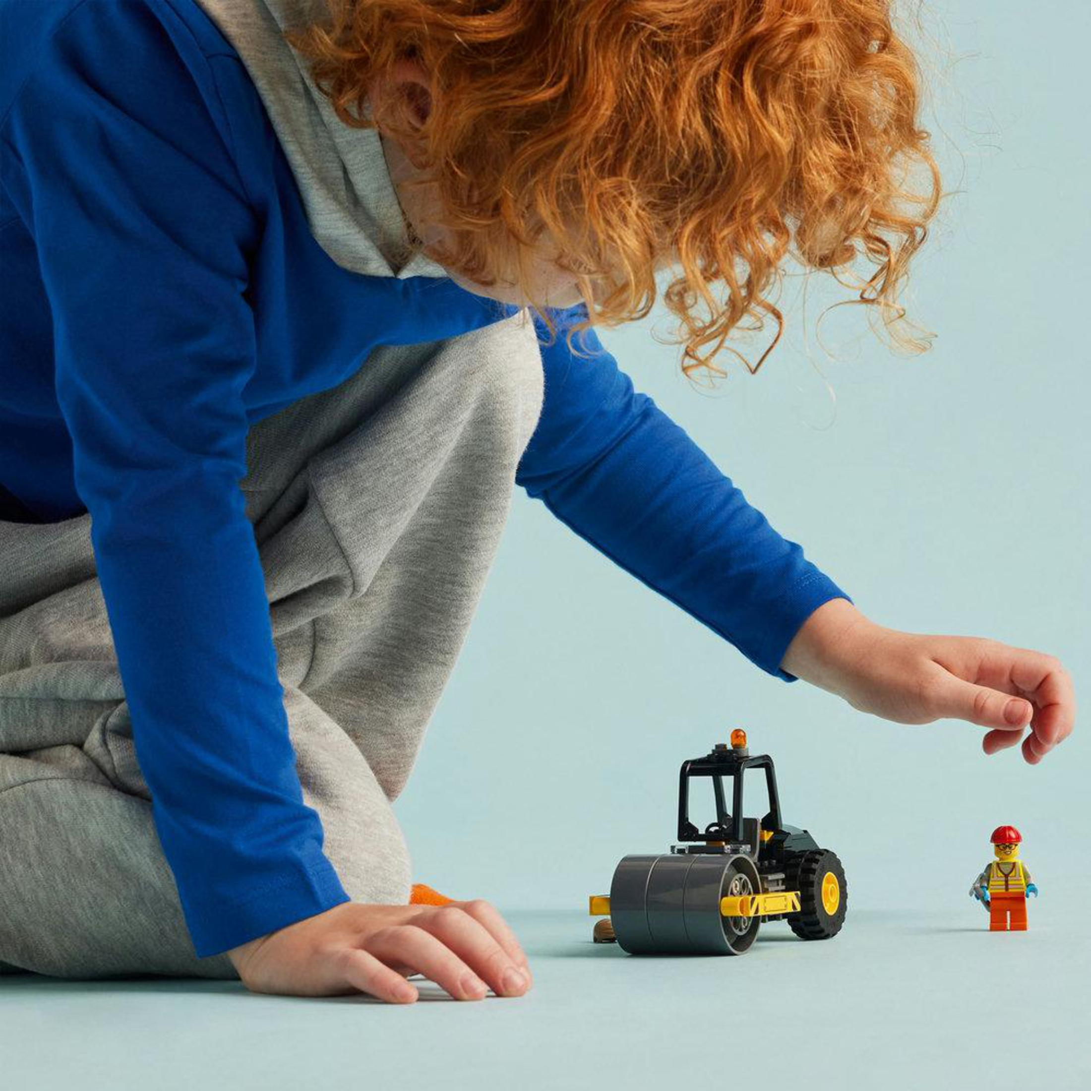 Een kind speelt met Lego bouwmachines. Een wals en een bouwvakker.