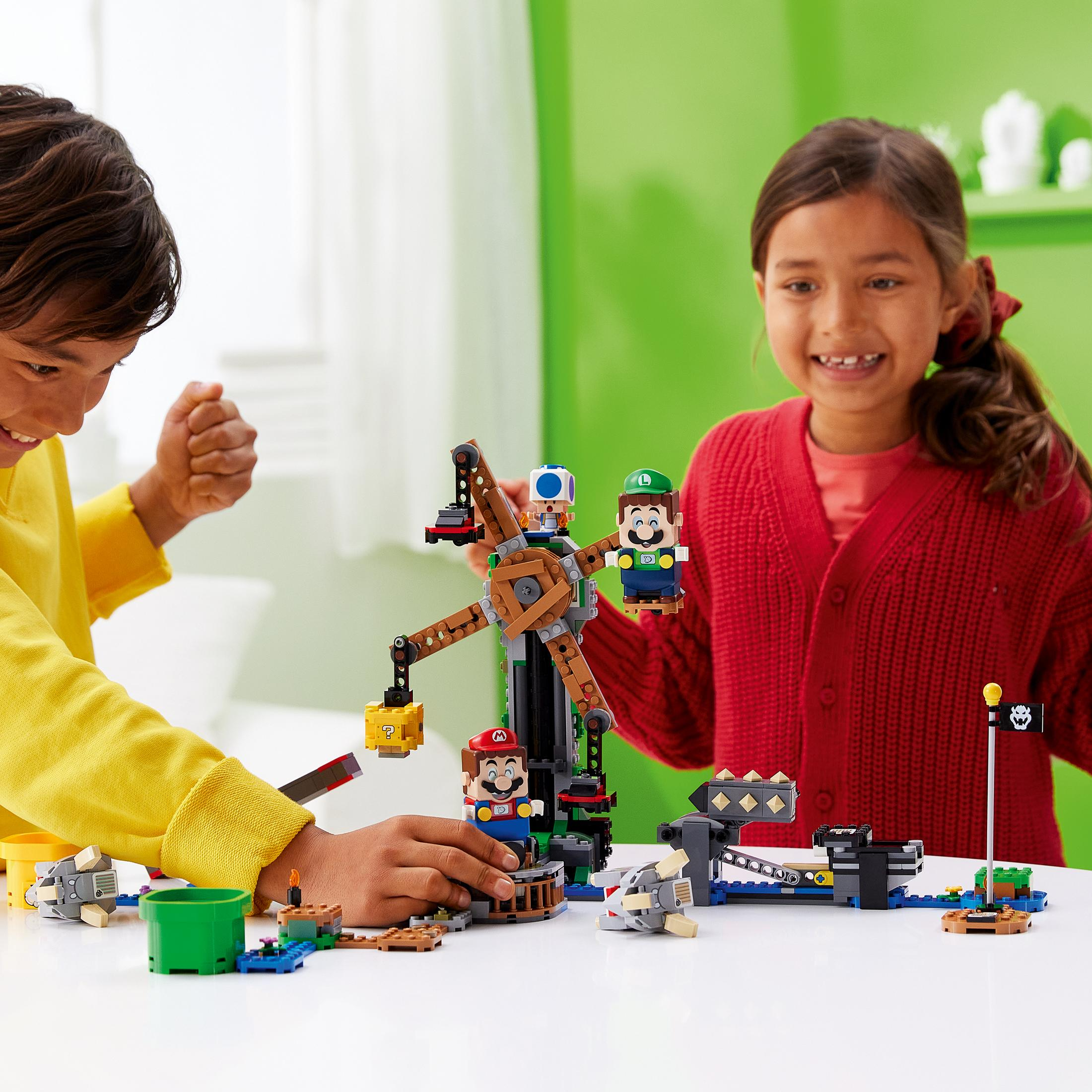 Zwei Kinder spielen mit einem LEGO-Set. Ein Riesenrad und LEGO-Figuren sind vorhanden. Der Hintergrund ist weiß.