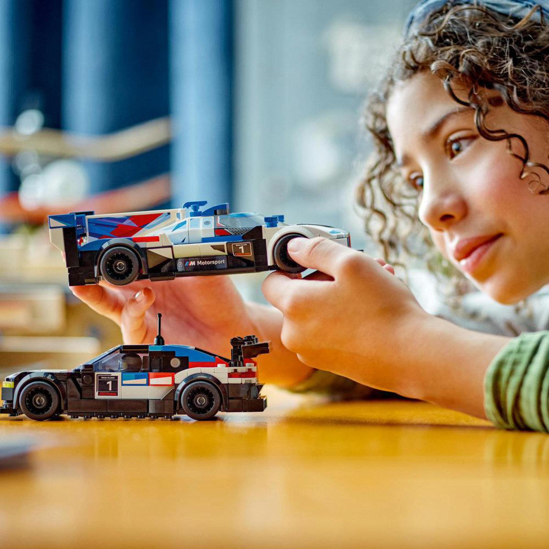 Een meisje dat twee Lego raceauto's voor haar gezicht houdt.