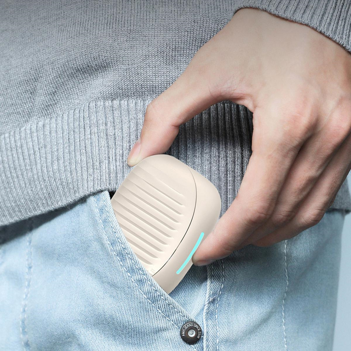 Person hält einen kleinen, cremefarbenen tragbaren Ventilator in einer Jeans-Tasche.