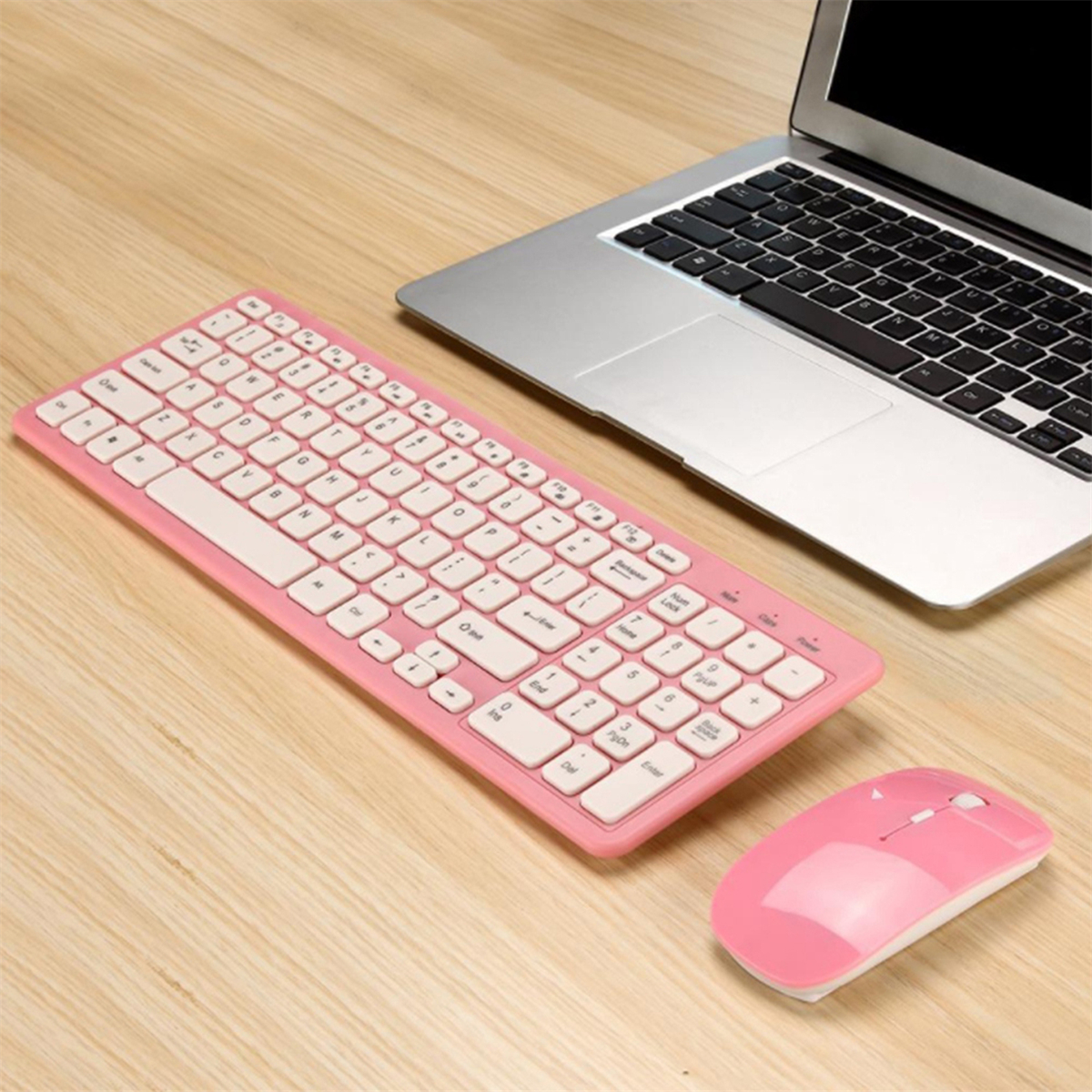 Rosa Tastatur, Maus und ein Laptop auf einem Holztisch. Weiße Tasten, silberner Laptop.