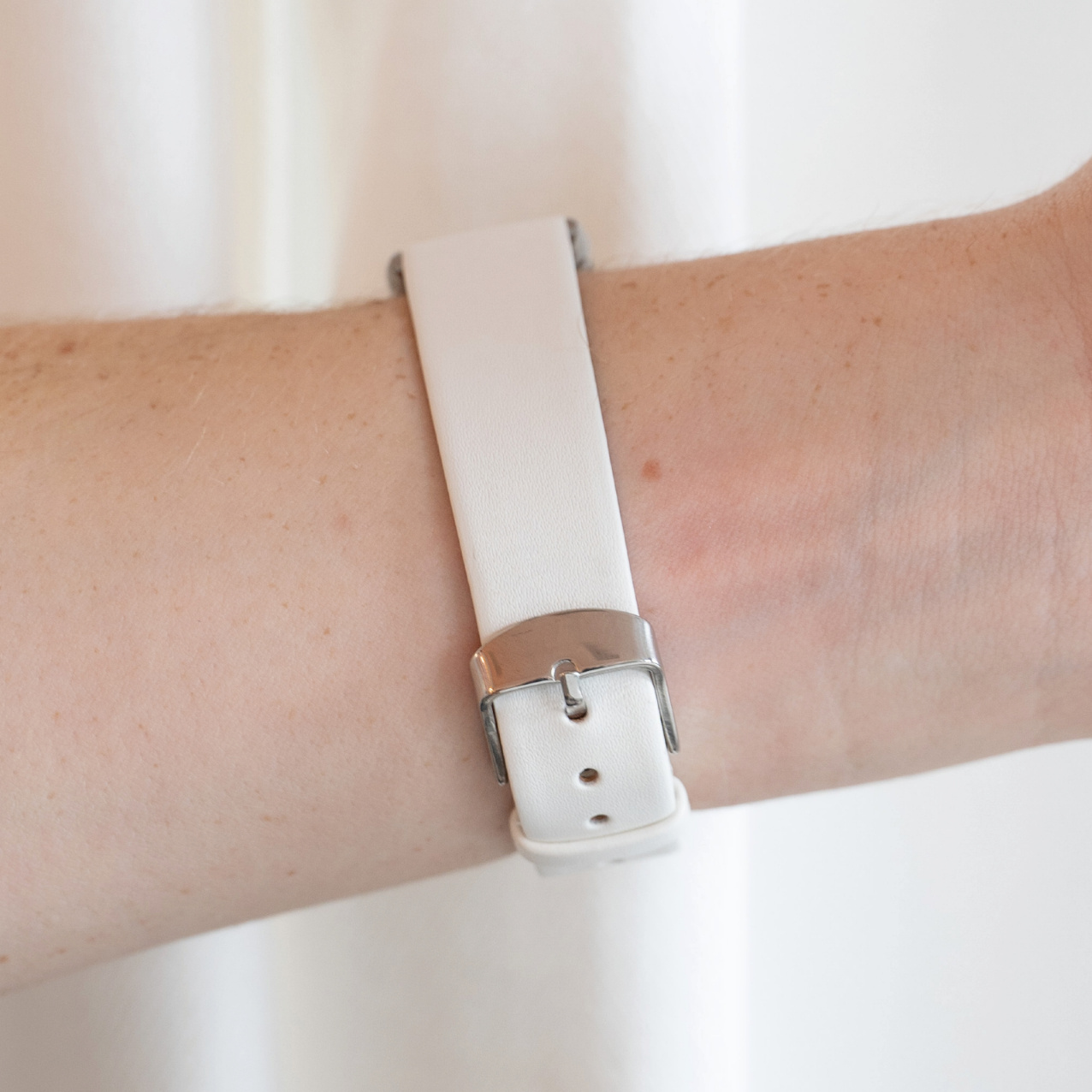 Ein Handgelenk mit einem weißen Uhrenarmband und einer silbernen Schnalle.