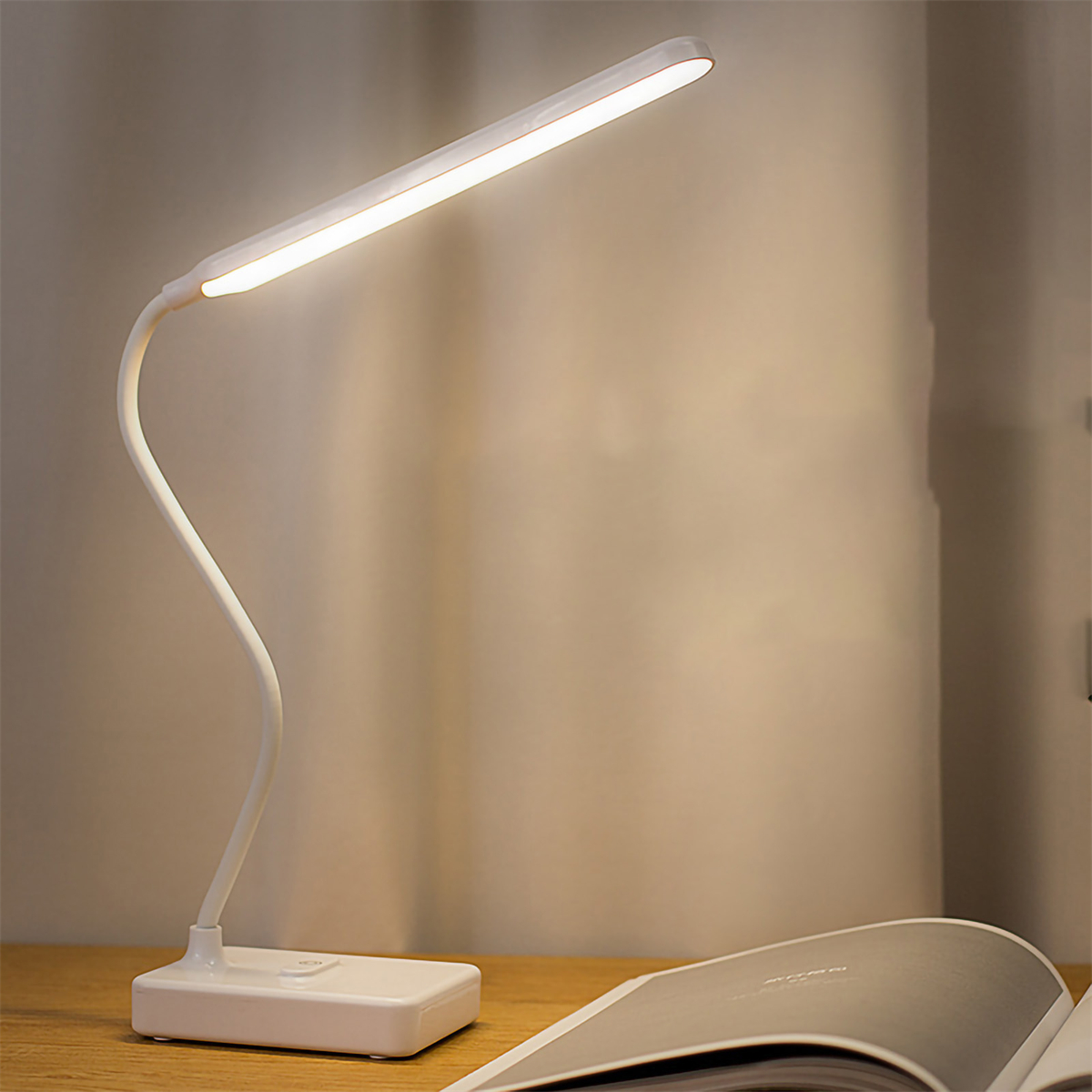 Eine weiße Schreibtischlampe mit gebogenem Hals, beleuchtet, auf einem Holztisch.