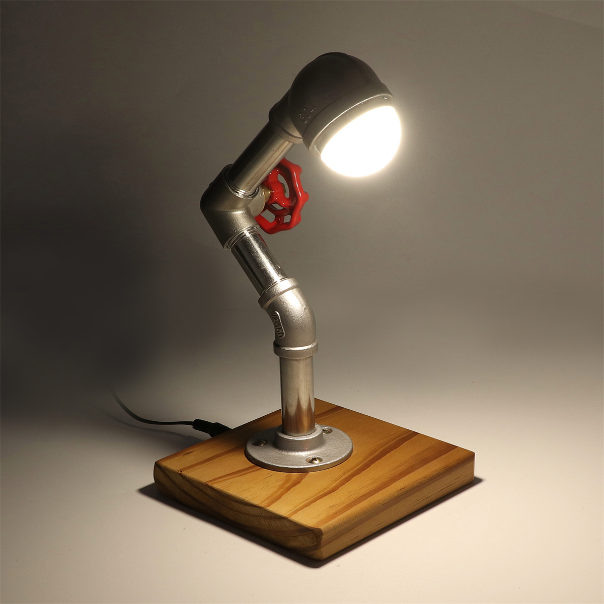 Eine Tischlampe aus Metallrohren mit rotem Ventil auf einem Holzsockel.