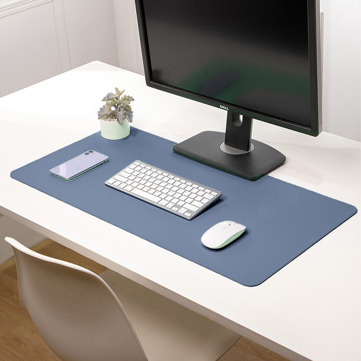 Schreibtisch mit Monitor, Tastatur, Maus, Telefon und kleiner Pflanze auf blauer Schreibtischunterlage.