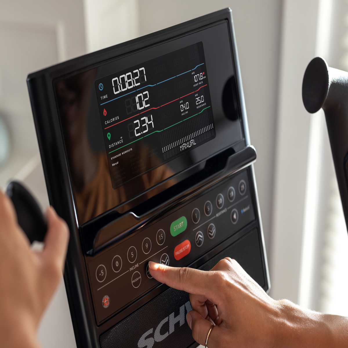 La mano di una persona preme un pulsante sul display di un tapis roulant. Lo schermo mostra statistiche e controlli.