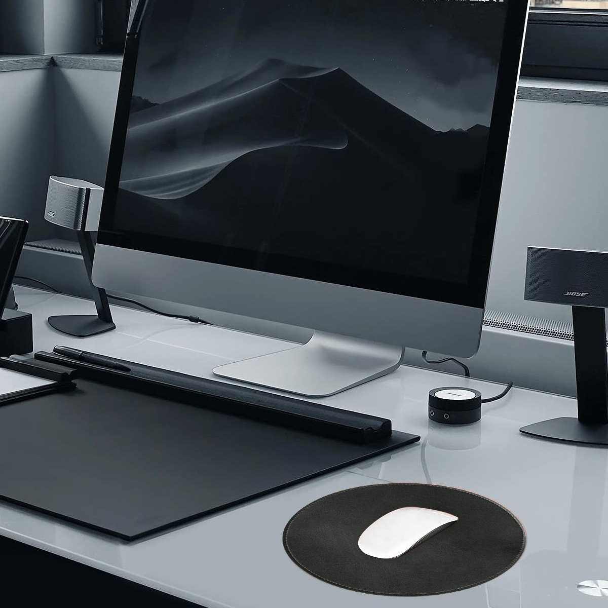 Ein schlanker Schreibtisch mit Monitor, Lautsprechern und einem Mauspad mit weißem Akzent.