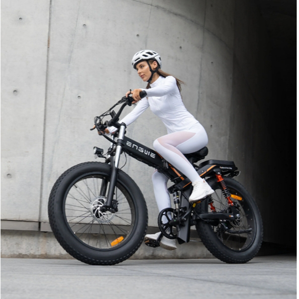 Kobieta na rowerze elektrycznym Ensue jedzie ulicą. Nosi biały strój i kask.