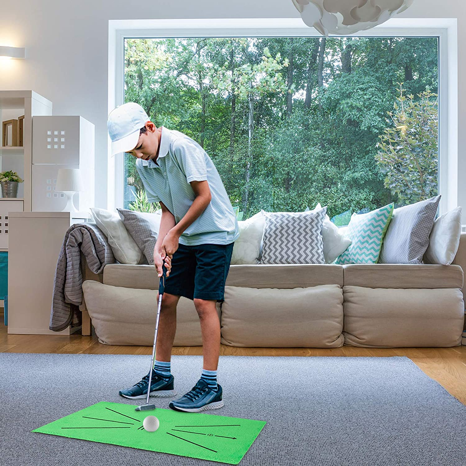 Ein Junge, der eine grüne Golfmatte auf einen grauen Teppich legt, mit Fensterhintergrund.