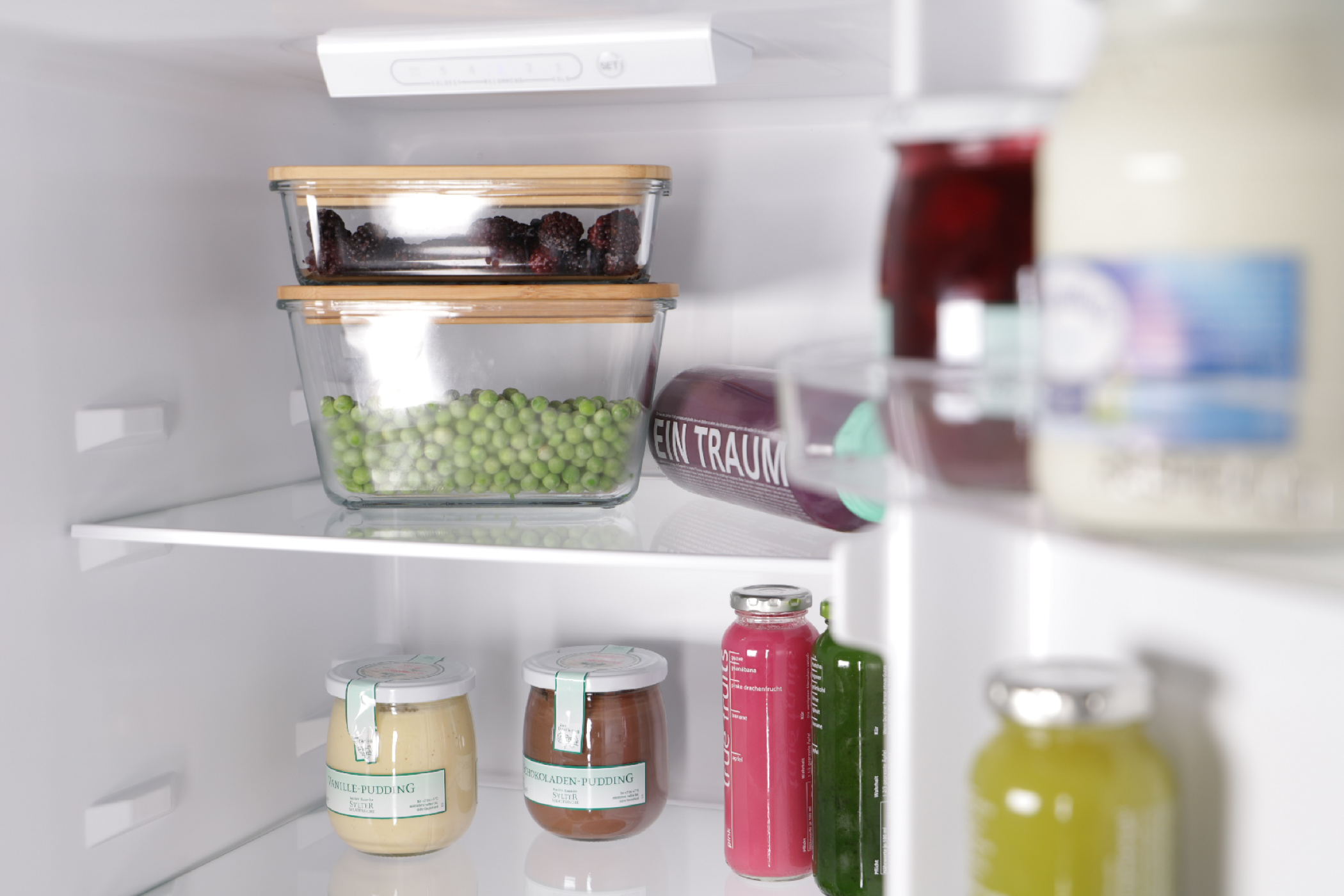 Offener Kühlschrank mit Glasbehältern mit Lebensmitteln. Es gibt Gläser und Flaschen.