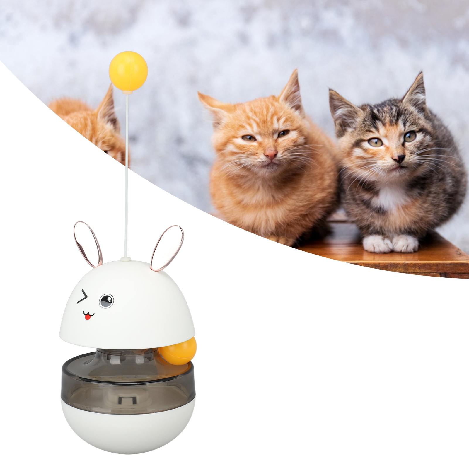 Ein weißes und graues Katzenspielzeug mit einem gelben Ball und drei Katzen im Hintergrund. Zwei Katzen sind orange, eine ist grau.