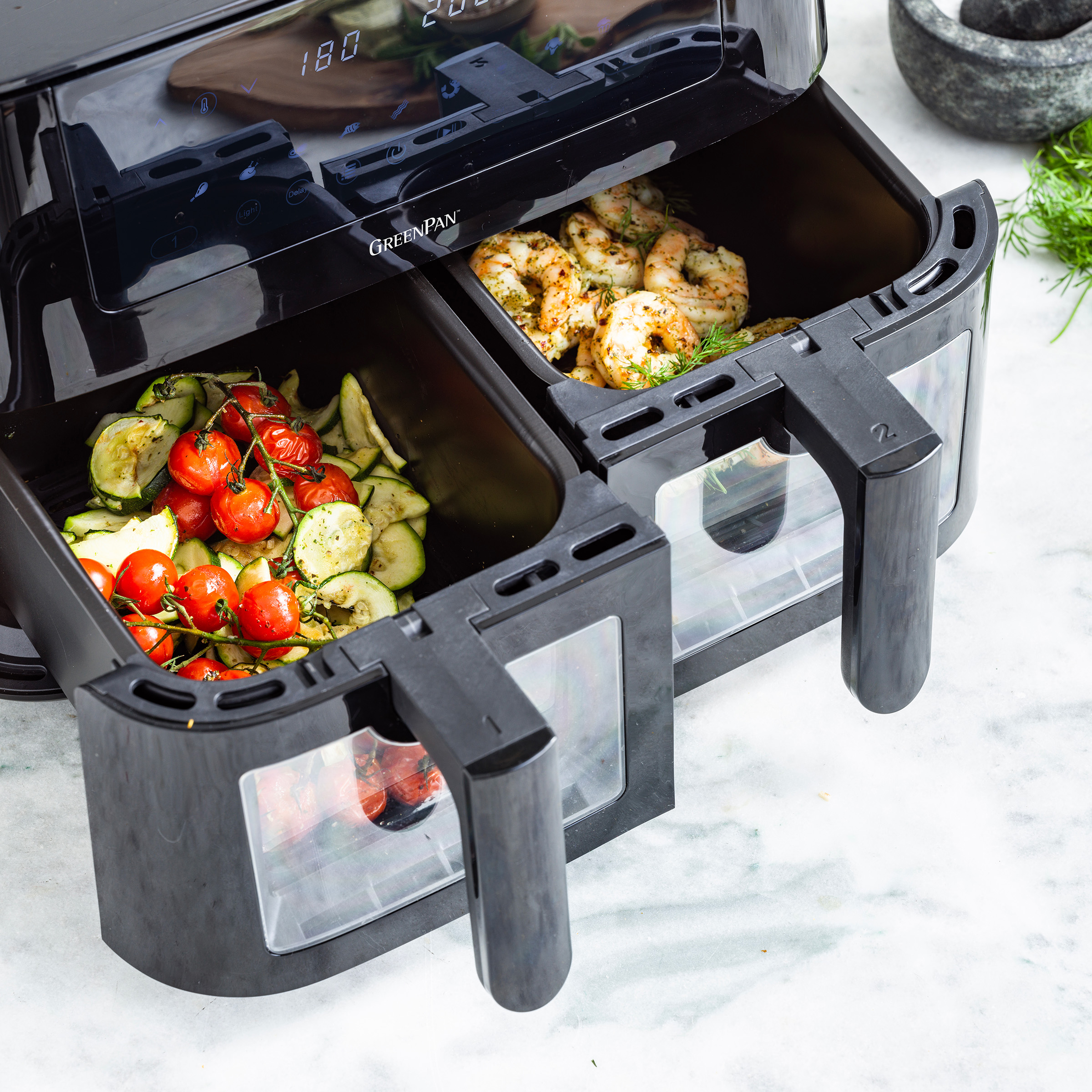 Schwarze Dual-Airfryer mit gekochtem Essen, Tomaten und Garnelen, auf Marmoroberfläche.