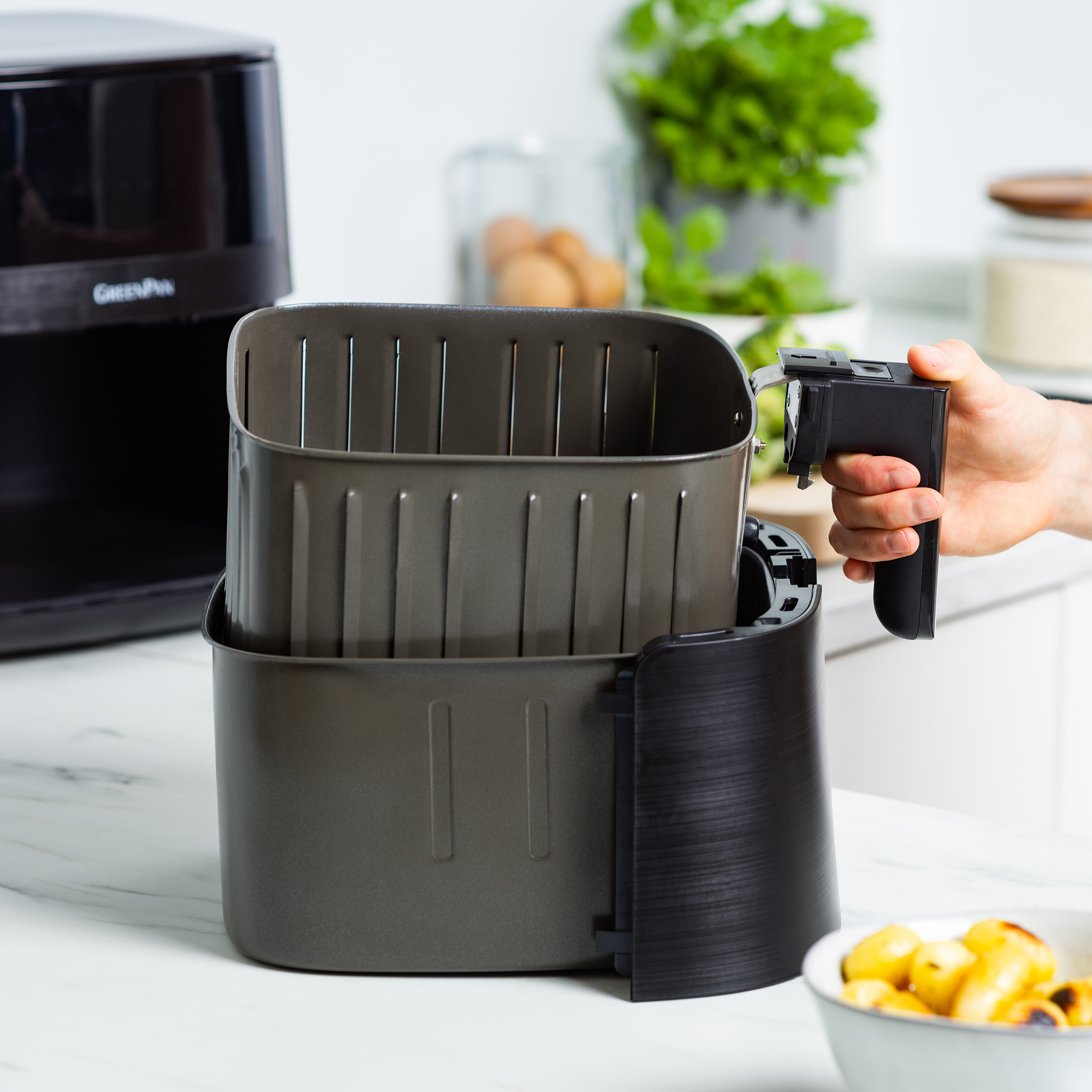 Una friggitrice ad aria con un cestello estratto da una persona. Sfondo cucina.