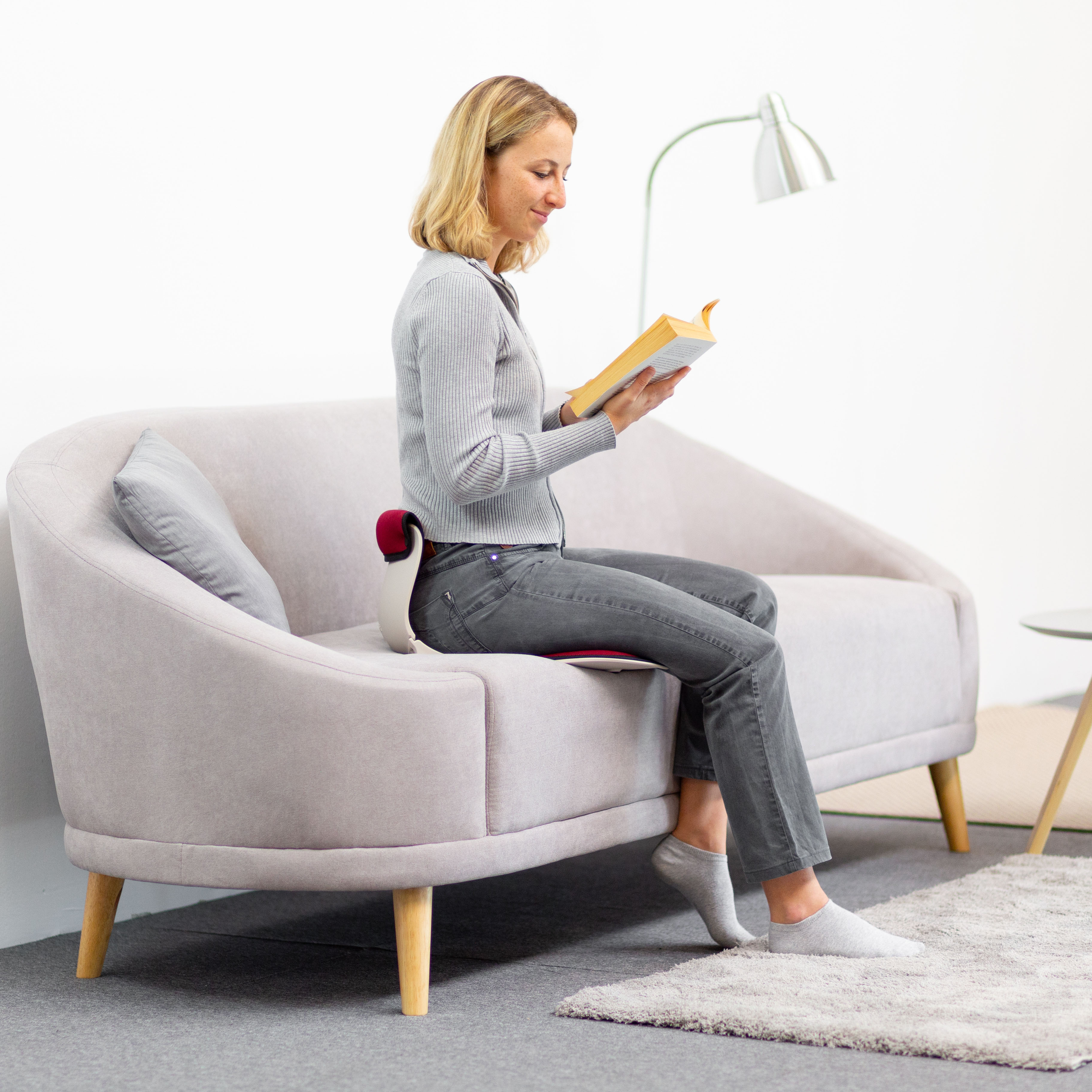 Frau liest ein Buch, sitzt auf einer Couch mit Rückenstützkissen.