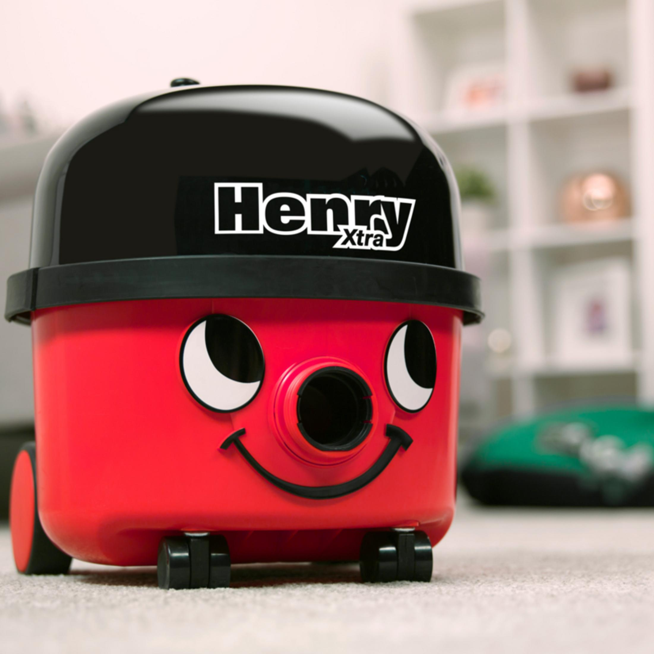 Ein roter und schwarzer Henry Staubsauger. Er hat ein lächelndes Gesicht und Räder. Das Wort 'Henry' steht darauf.