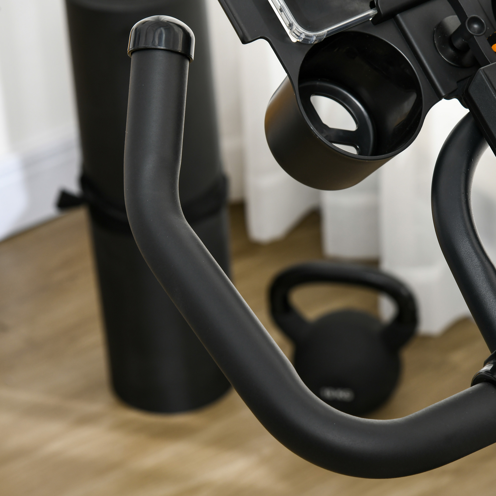Manubrio nero della cyclette, portaborraccia e kettlebell, su pavimento in legno.