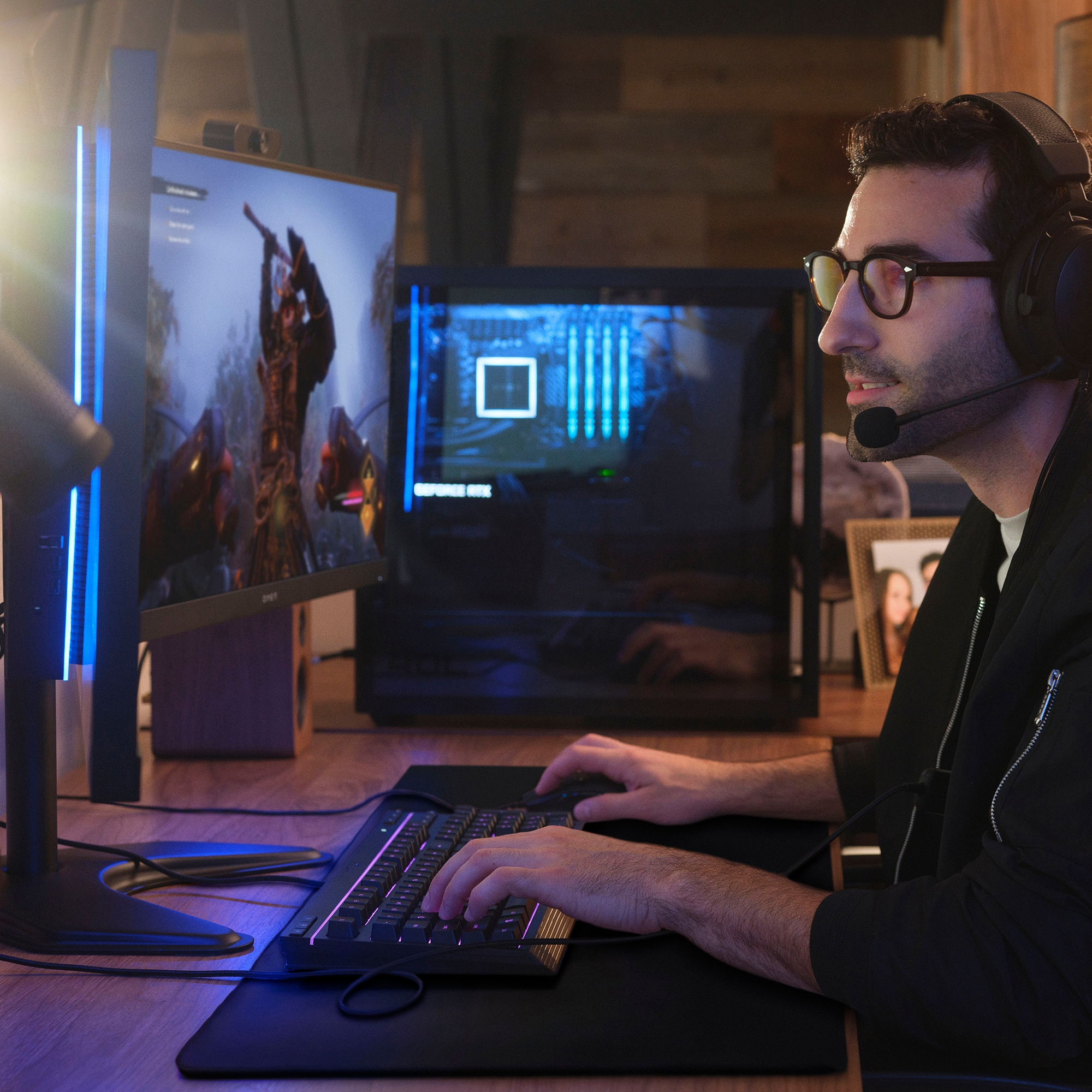 Mężczyzna w okularach i zestawie słuchawkowym grający na komputerze z podświetlaną klawiaturą.