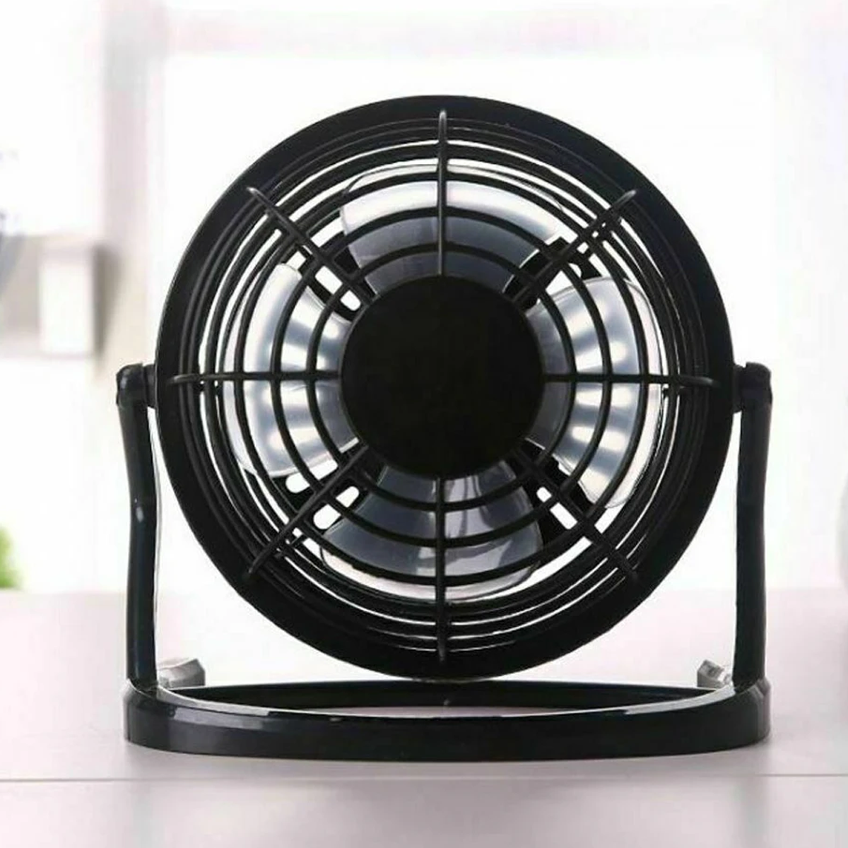 Ein kleiner, schwarzer, runder Ventilator mit Schutzgitter, der auf einer weißen Oberfläche steht.