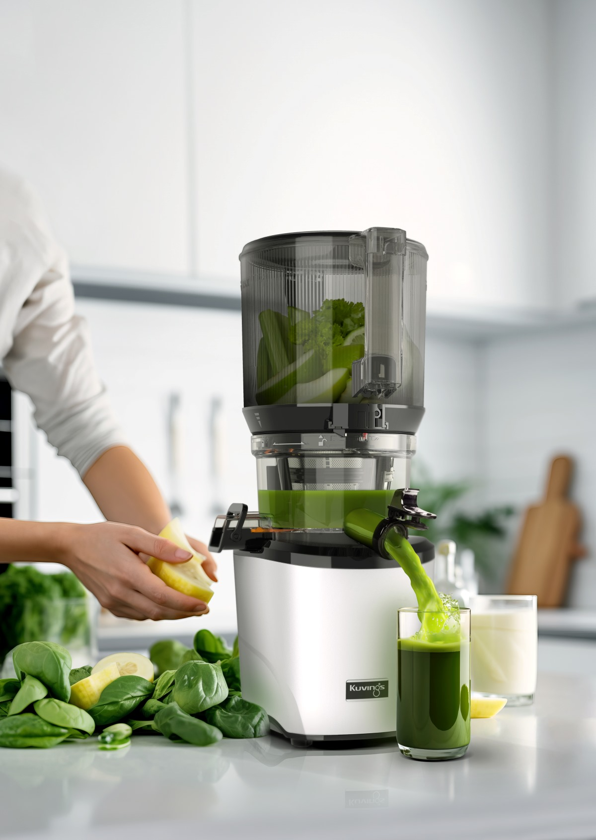 Persona exprimiendo con una exprimidora; jugo verde vierte en vaso, espinacas y limón cerca.