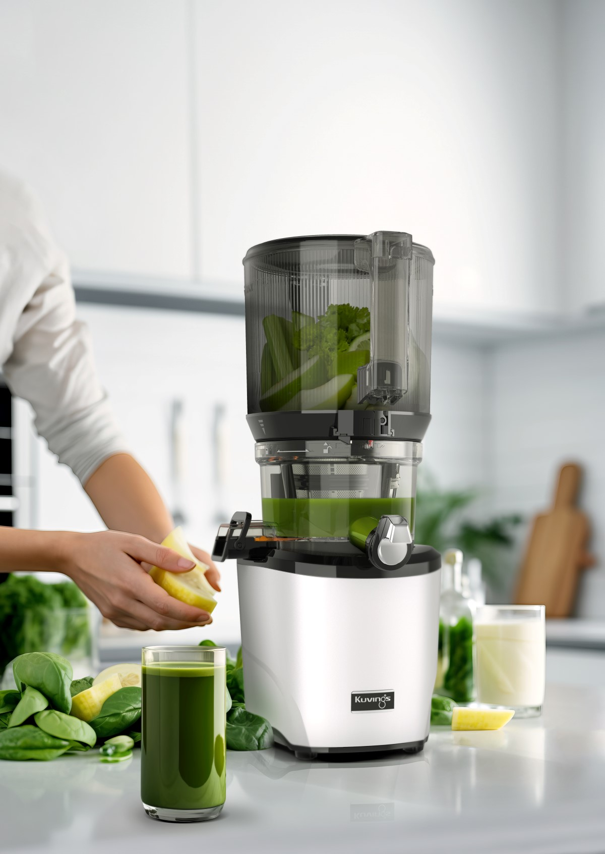 Una mujer exprimiendo jugo con una exprimidora plateada y negra, los ingredientes son visibles, con un vaso de jugo.