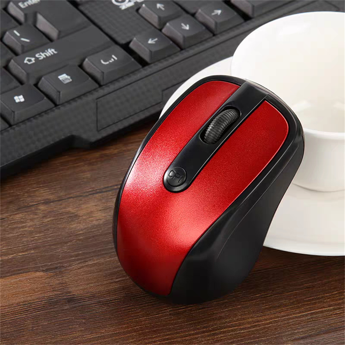 Eine rot-schwarze Computermaus auf einem Holzschreibtisch. Eine Tastatur und eine weiße Tasse befinden sich im Hintergrund.