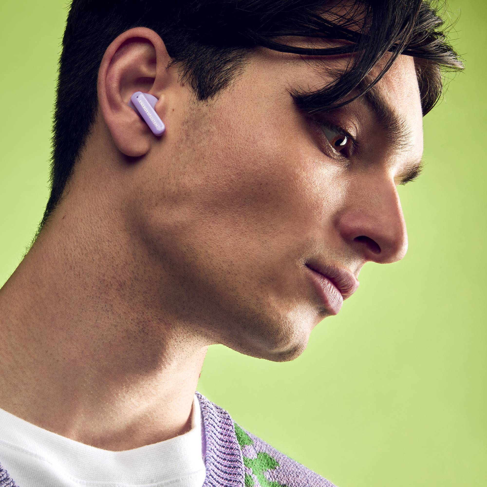 Een man met een lila trui, met een paarse in-ear koptelefoon in zijn oor.