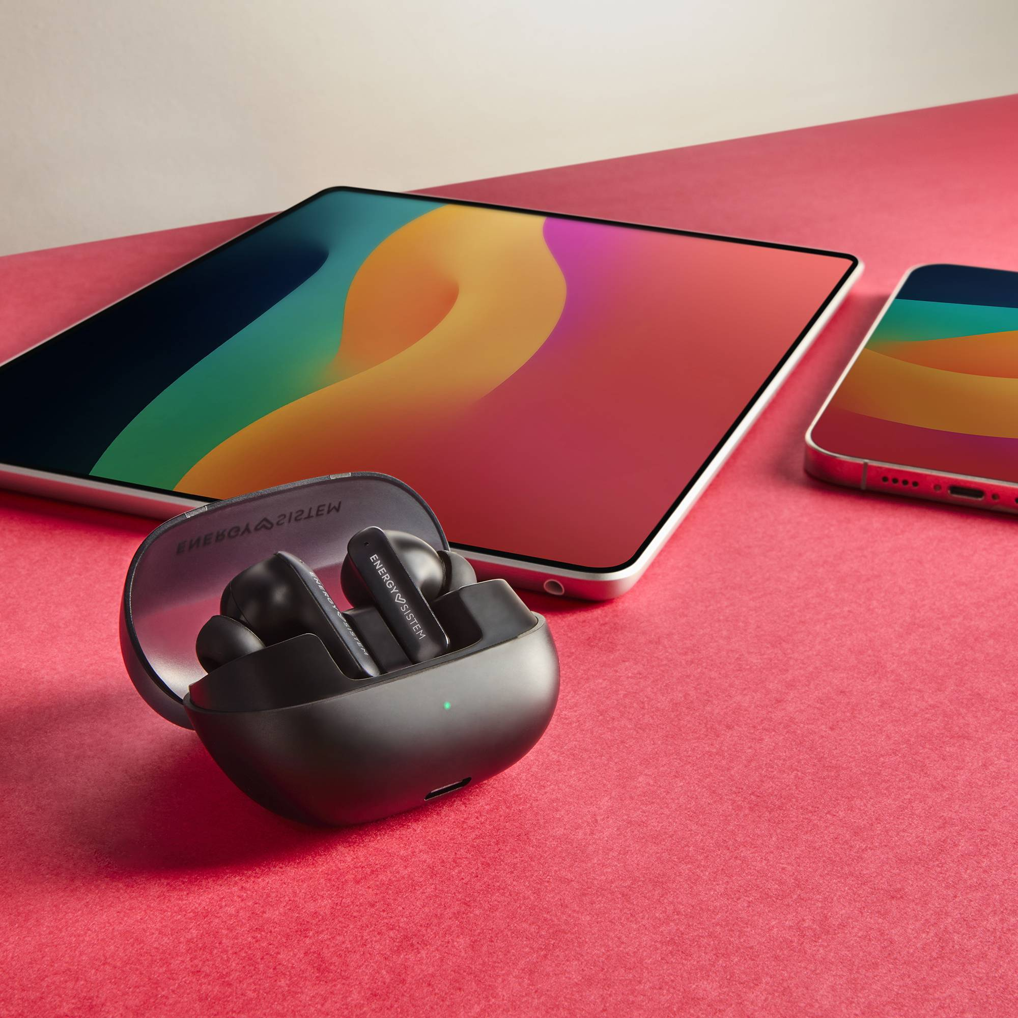 Ohrhörer, Tablet und Telefon auf roter Oberfläche. Ohrhörer in Ladecase.