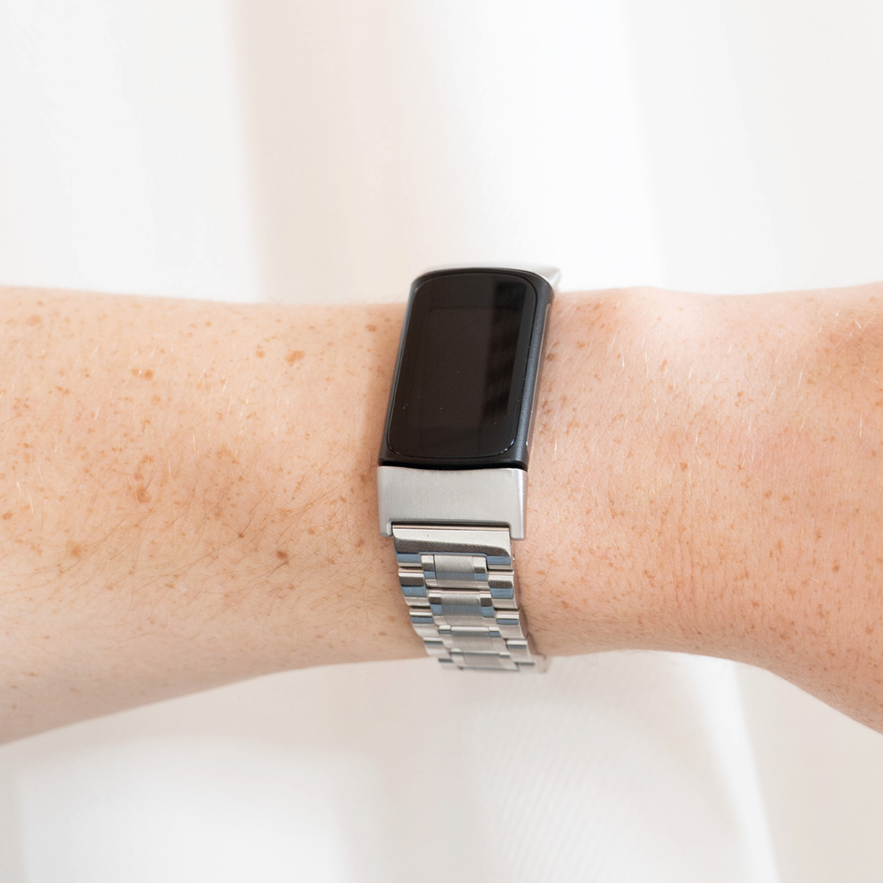Eine silberne Smartwatch mit schwarzem Bildschirm befindet sich an einem Handgelenk.