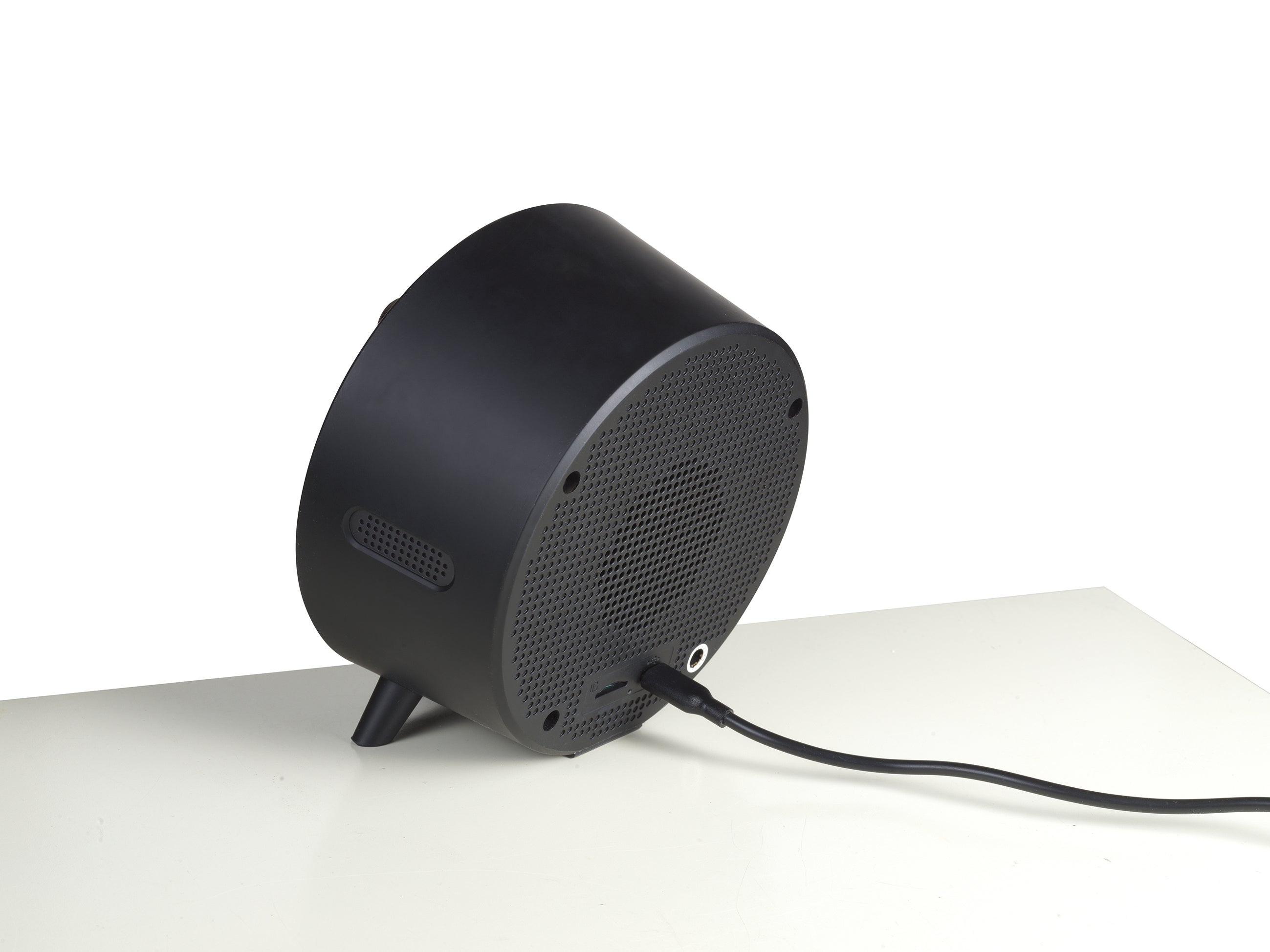 Altavoz negro con cable enchufado. El altavoz está sobre una superficie blanca.
