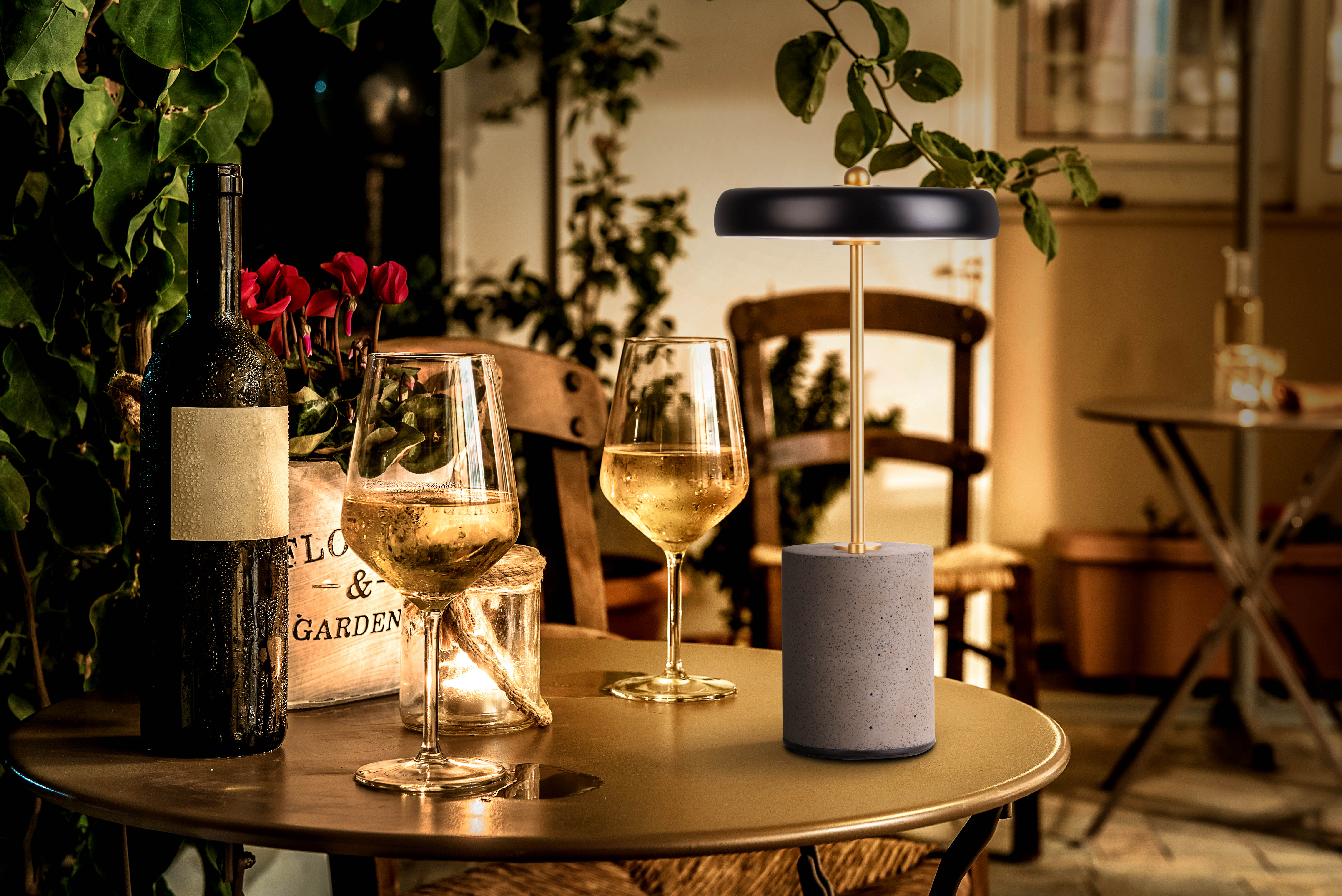 Tisch mit Weinflasche, Gläsern, Lampe und Blumen, Abendessen im Freien.