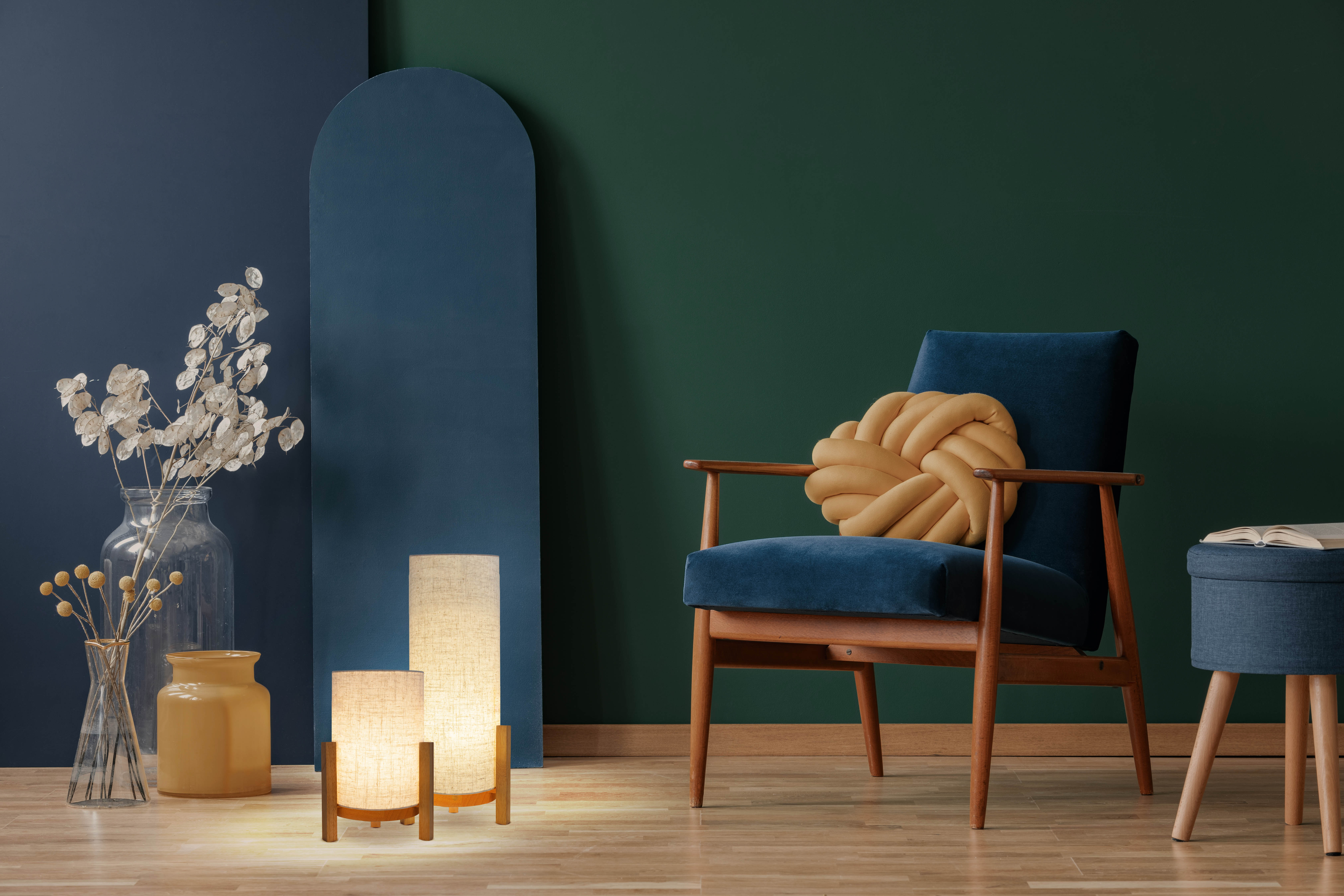 Ein Raum mit blauem Stuhl, Lampe und Vase, mit dunkelgrüner Wand.