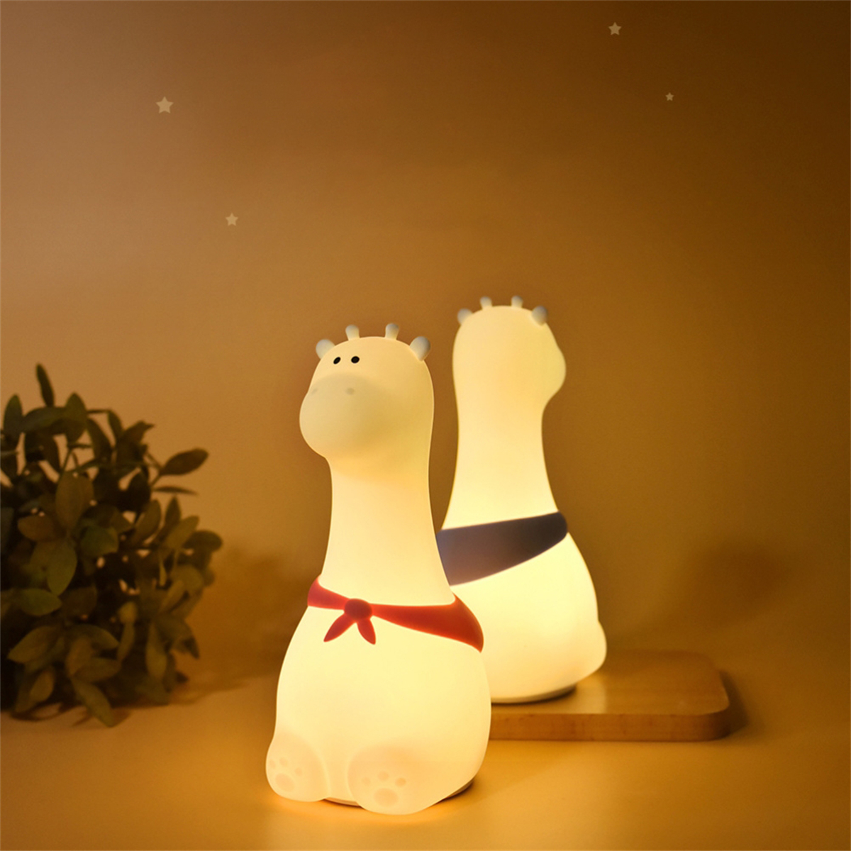 Zwei giraffenförmige Nachtlichter. Eines hat eine rote Fliege. Der Hintergrund ist warm und neutral.
