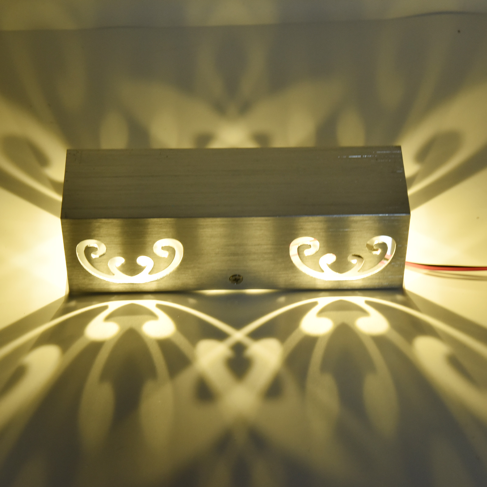 Silberne Wandlampe mit dekorativen Mustern und Lichtreflexionen.