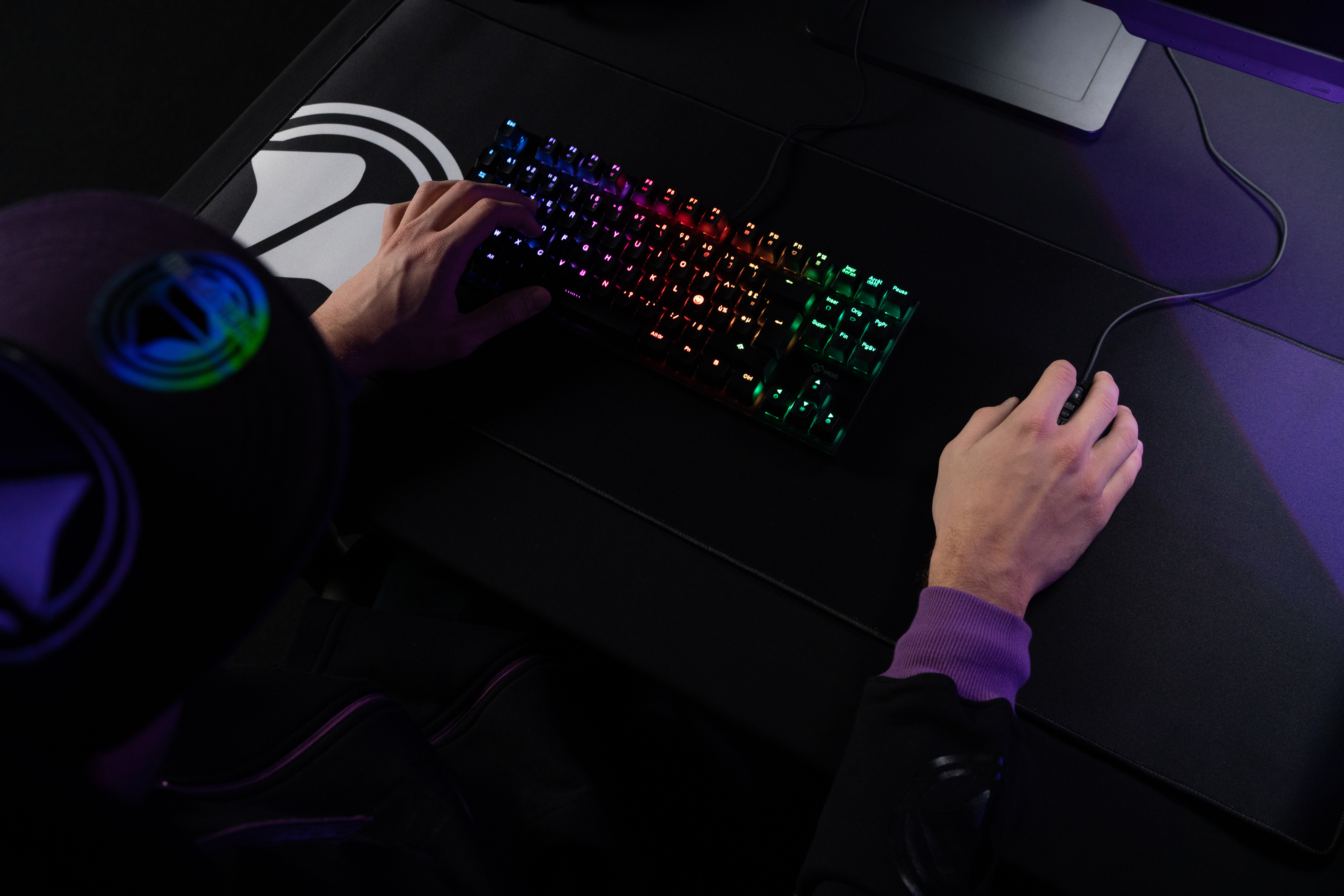 Hände einer Person auf einer Gaming-Tastatur mit bunten, beleuchteten Tasten, Maus und Matte im Blick.