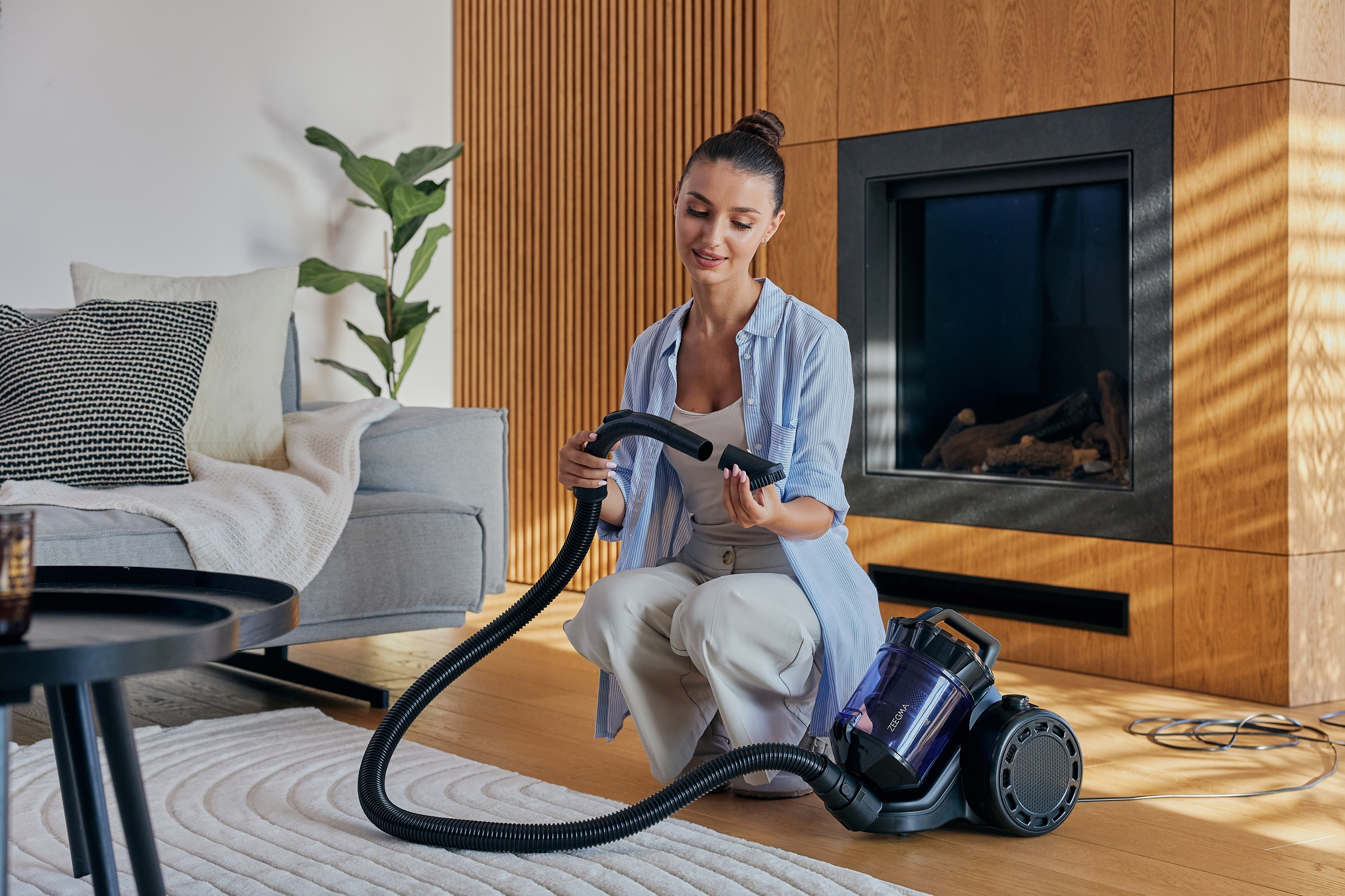 Kobieta odkurzająca salon odkurzaczem, uśmiechnięta, z dywanem i meblami.