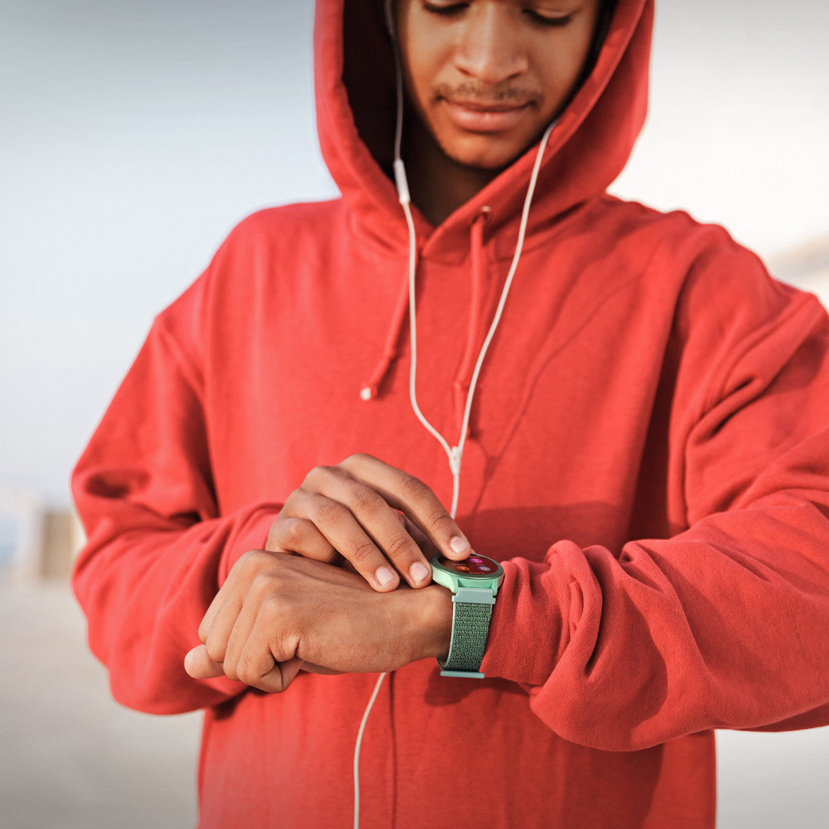 Hombre con sudadera roja mirando un reloj inteligente, con auriculares.