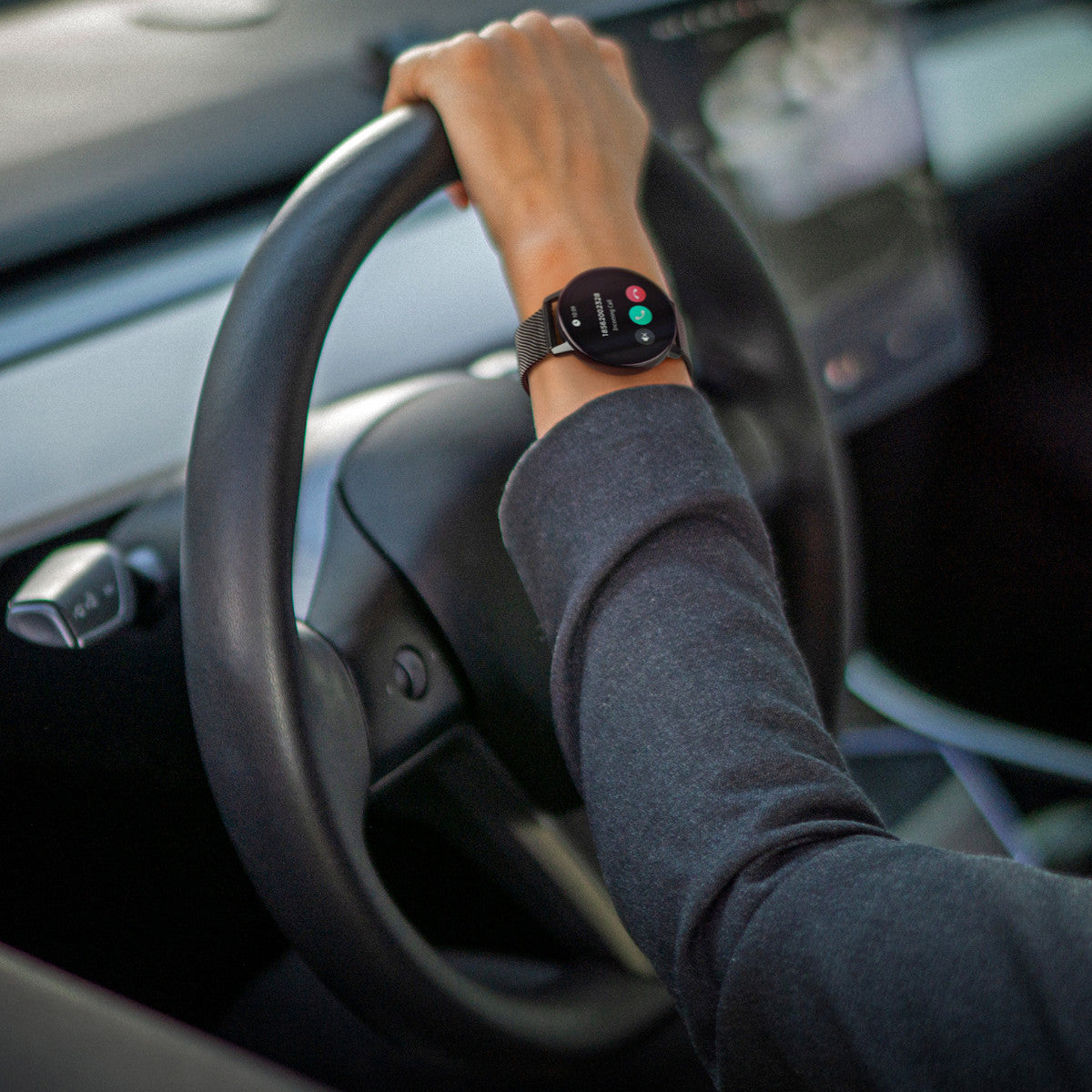 Polso di una persona con smartwatch che mostra informazioni sulle chiamate mentre guida un'auto.