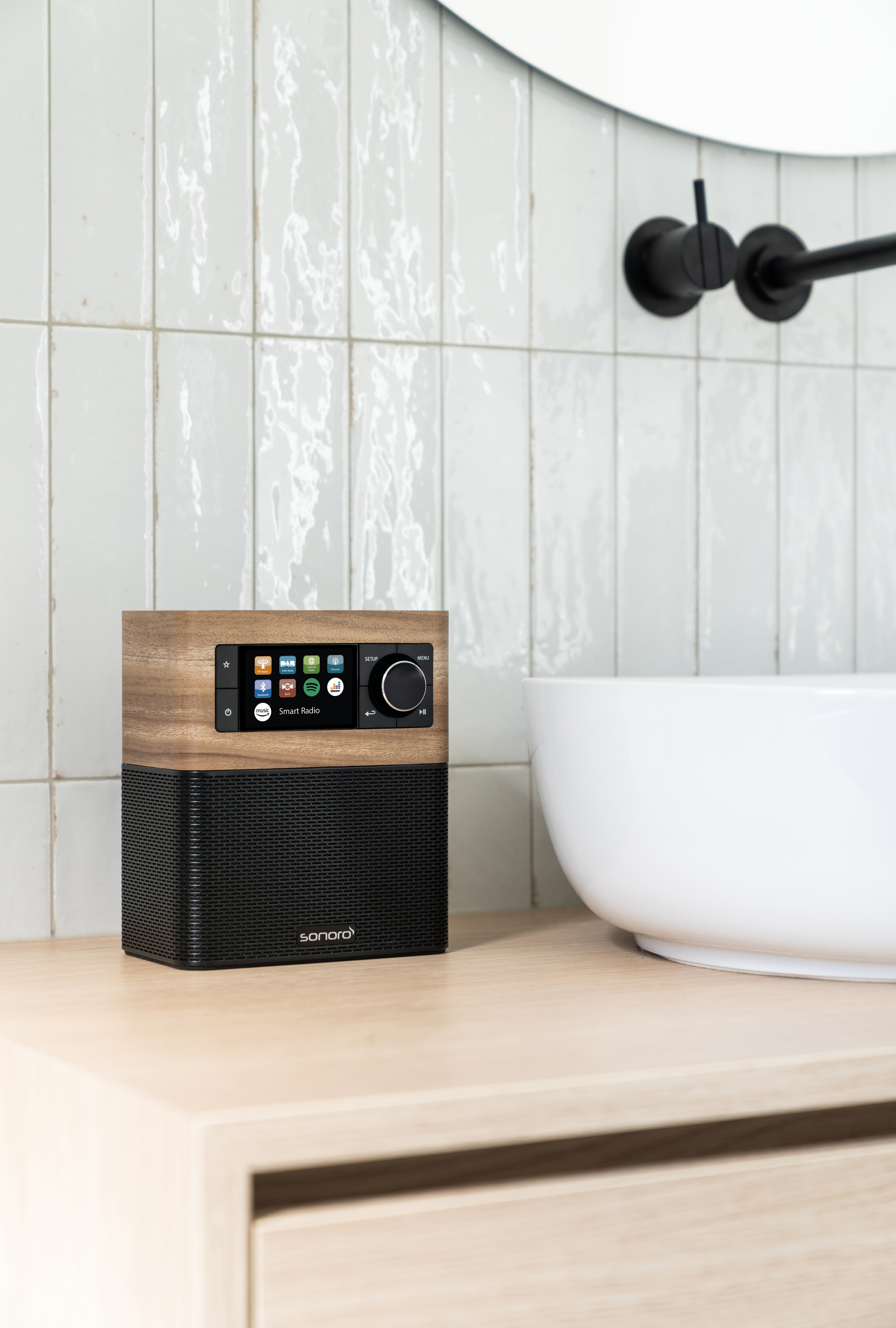 Smart-Radio mit Holzoberteil und schwarzem Netz. Auf einem Holzregal im Badezimmer platziert.