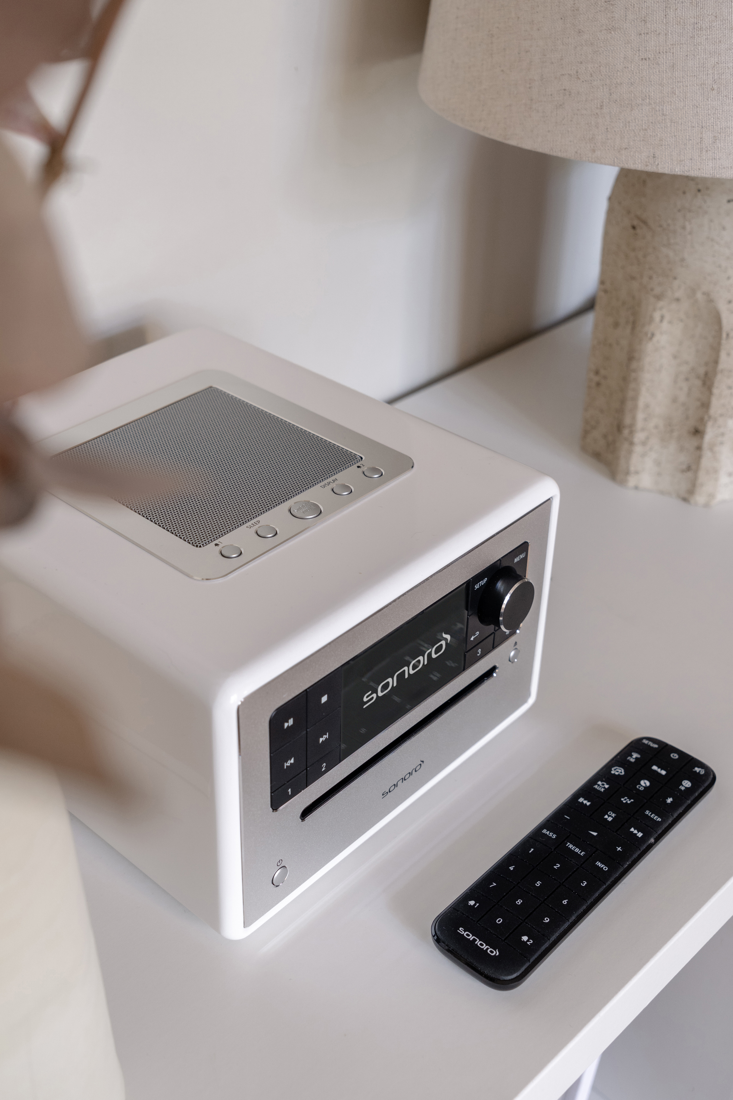 Witte smart radio met een afstandsbediening op een witte tafel. De radio heeft een scherm.