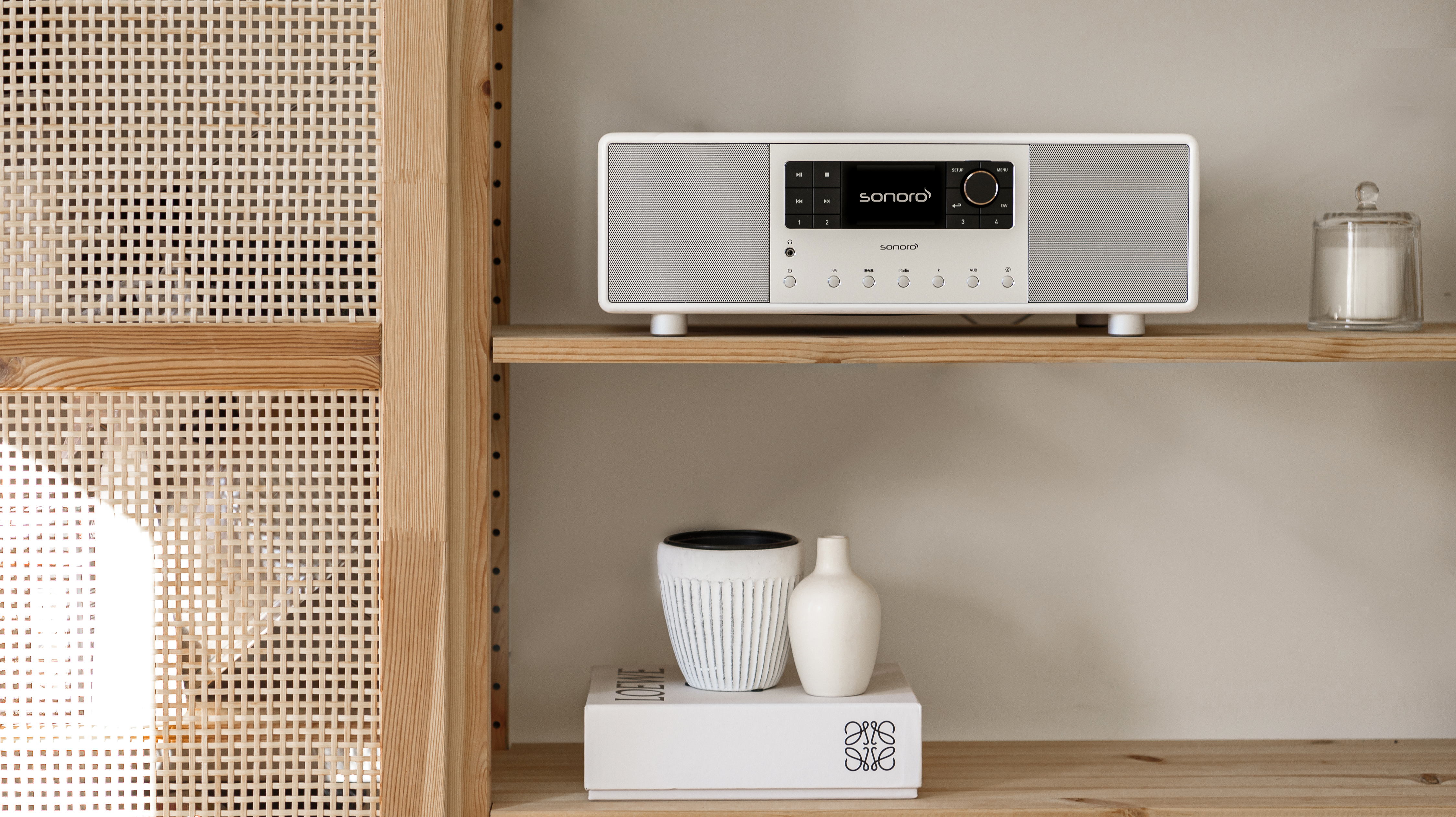 A white audio system on a wooden shelf, with decorative items on the shelf, in a room.