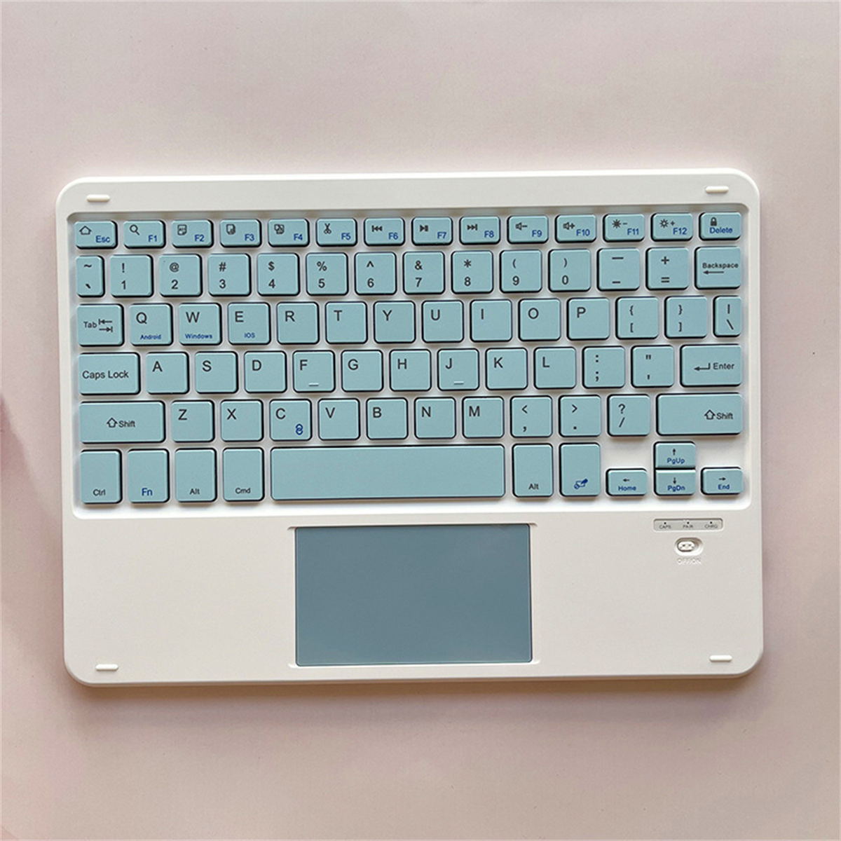 Eine weiße Tastatur mit hellblauen Tasten und einem Touchpad auf rosa Oberfläche.
