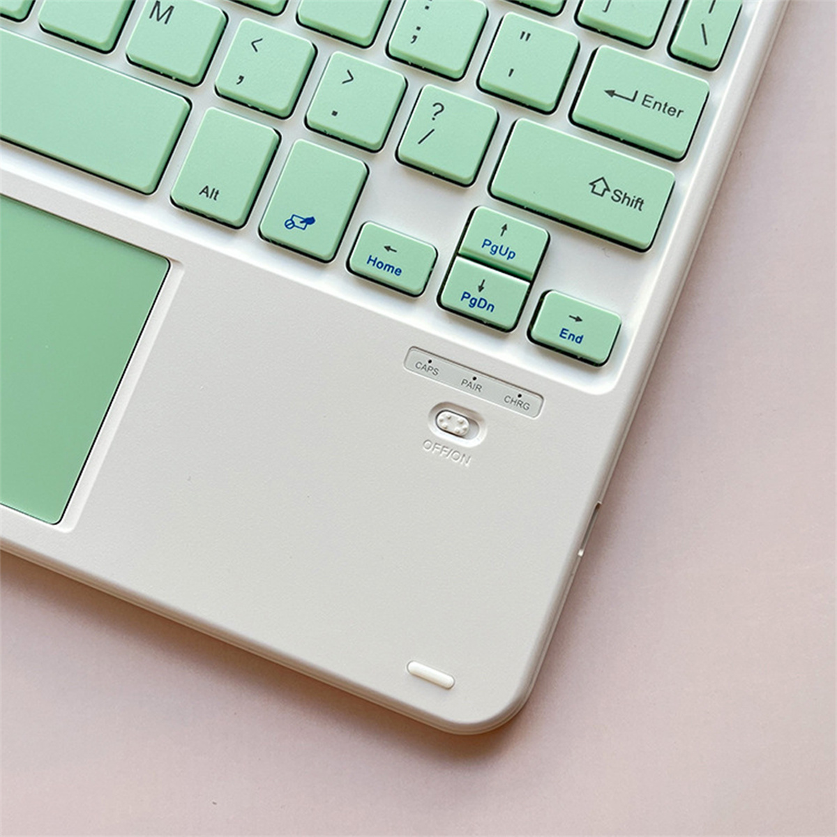 Eine weiße und grüne Tastatur mit Touchpad und Funktionstasten auf einer rosa Oberfläche.