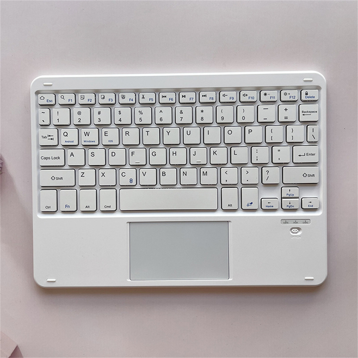 Eine weiße kabellose Tastatur mit Touchpad und eine Nahaufnahme der Tasten. Sie liegt auf einer rosa Oberfläche.