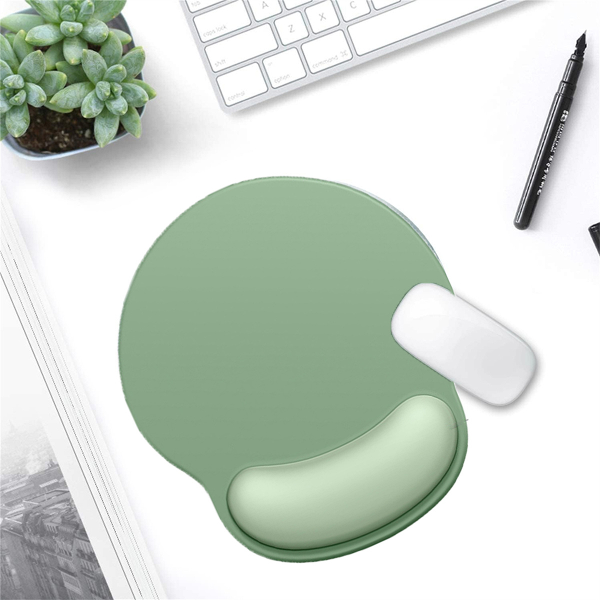 Grünes ergonomisches Mauspad mit weißer Maus, Pflanze und Stift auf weißem Schreibtisch.