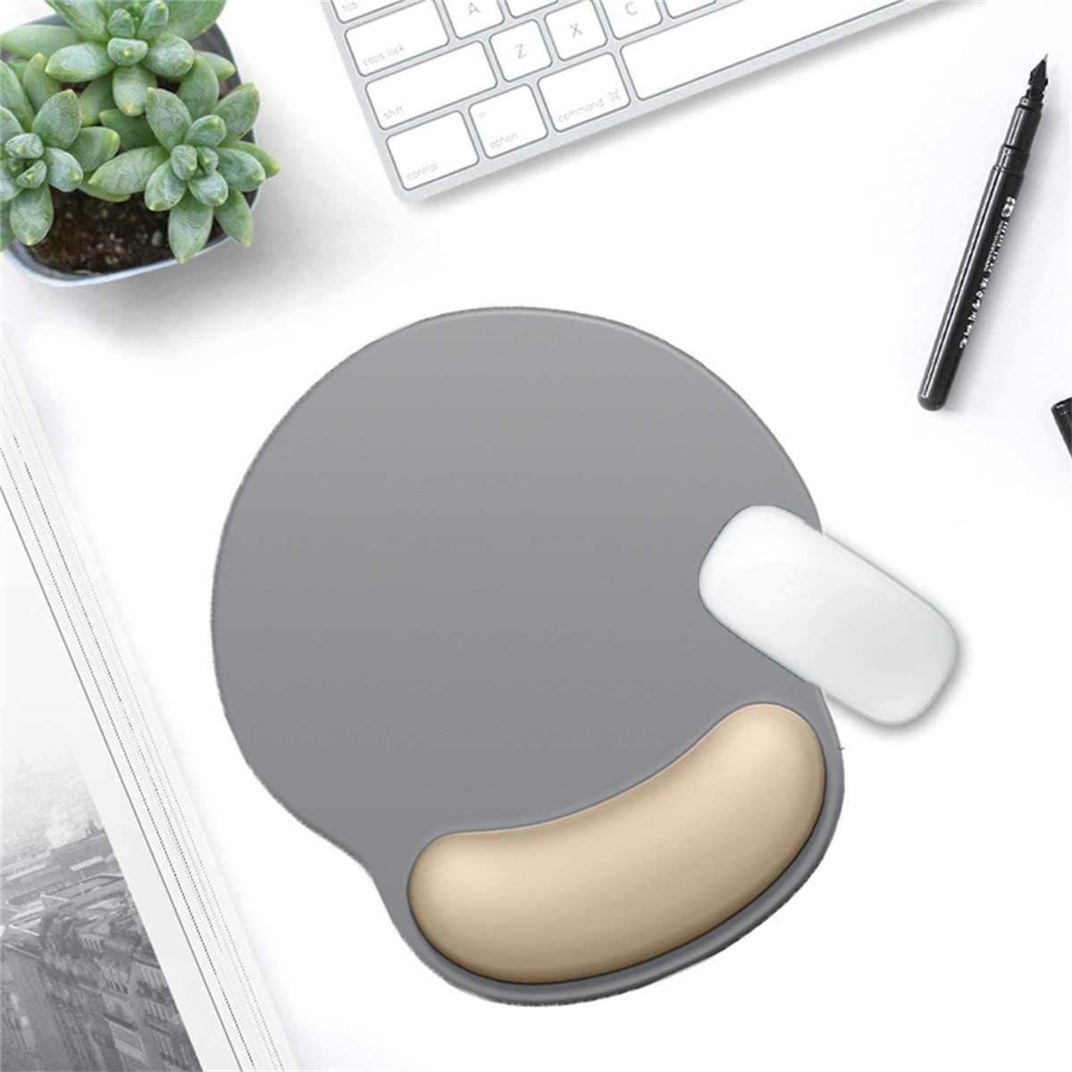 Ein graues Mauspad mit beiger Handballenauflage, eine weiße Maus, eine Tastatur und ein Stift auf einem weißen Schreibtisch.
