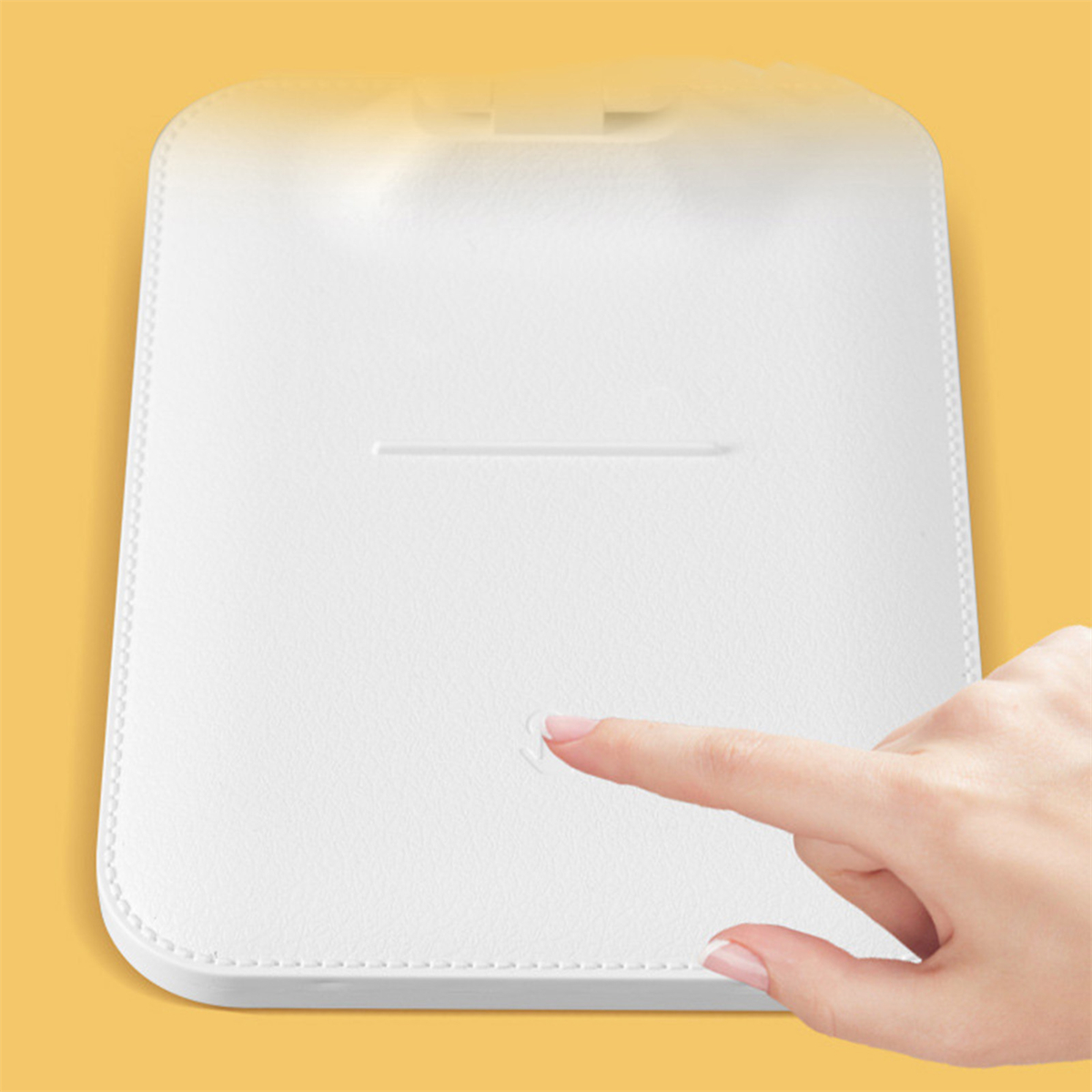 Eine Hand berührt ein weißes Pad auf gelbem Hintergrund. Es scheint ein Tablet oder ein ähnliches Gerät zu sein.