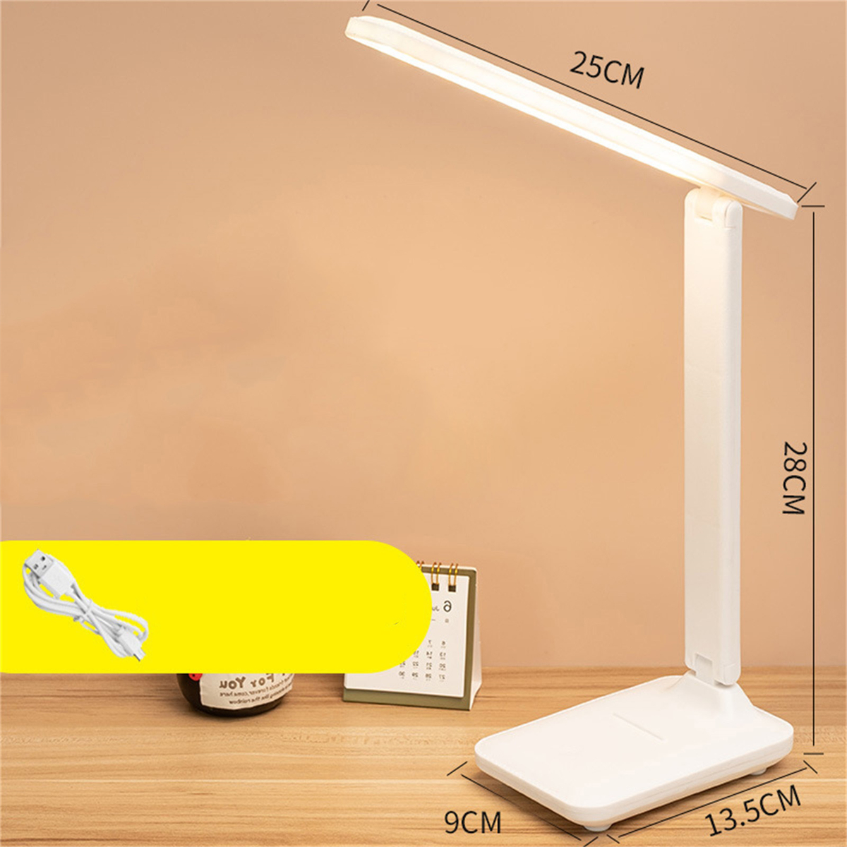 Eine weiße Schreibtischlampe. Sie steht auf einem Holztisch. Die Lampe ist an und die Abmessungen sind angegeben.