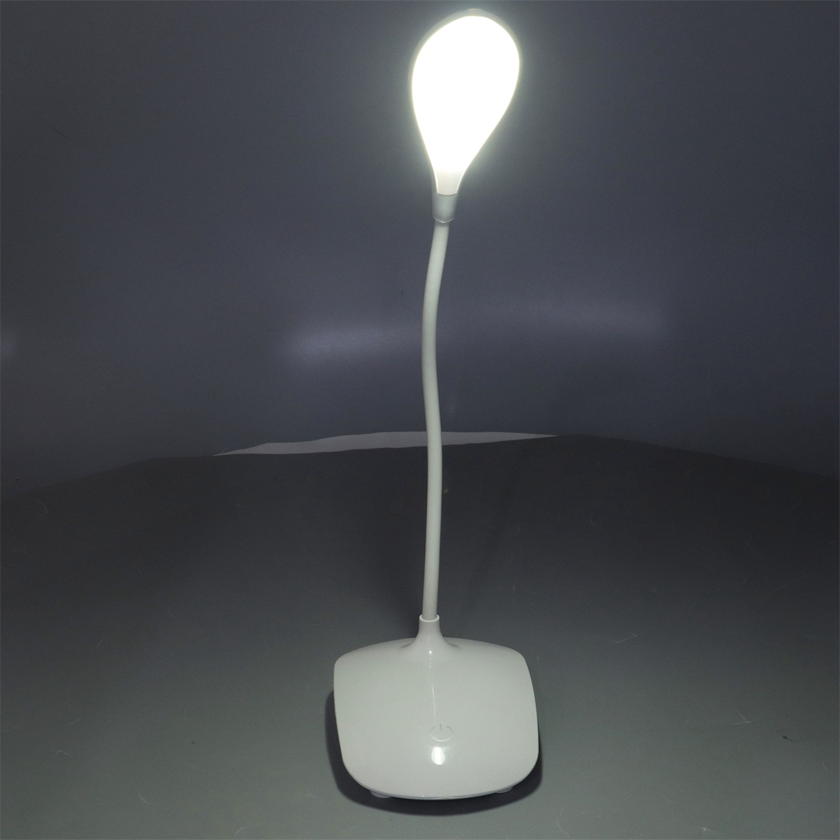 Weiße, moderne Schreibtischlampe mit gebogenem, leuchtendem Licht und weißem Sockel auf grauem Untergrund.